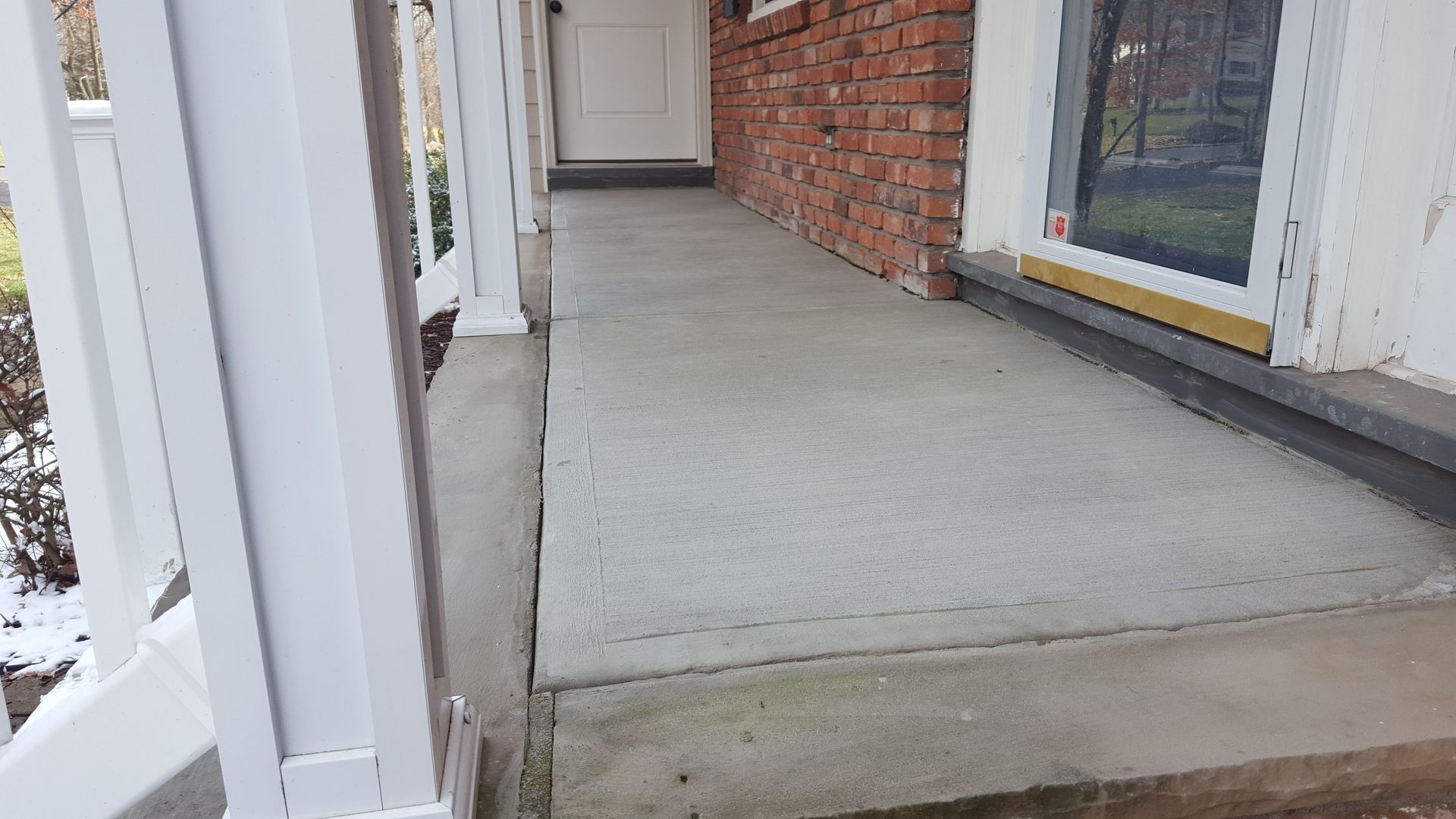 Concrete front porch with white railing, brick wall, and a window on the right.