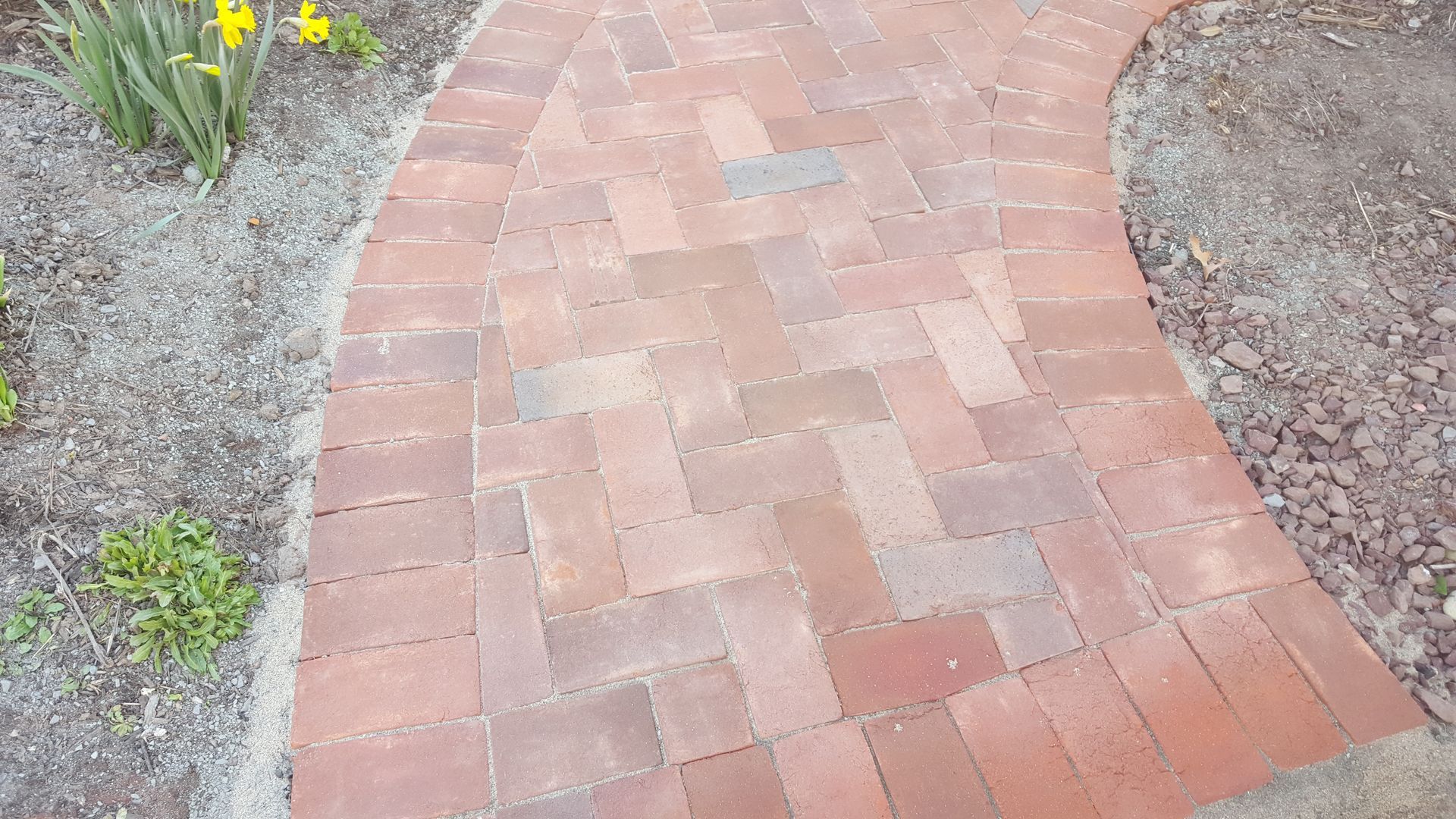 Curved red brick garden path bordered by gravel and small plants