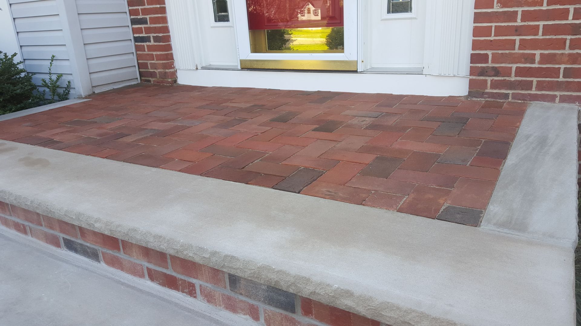 Brick front porch with a concrete step and white front door with a yellow welcome mat