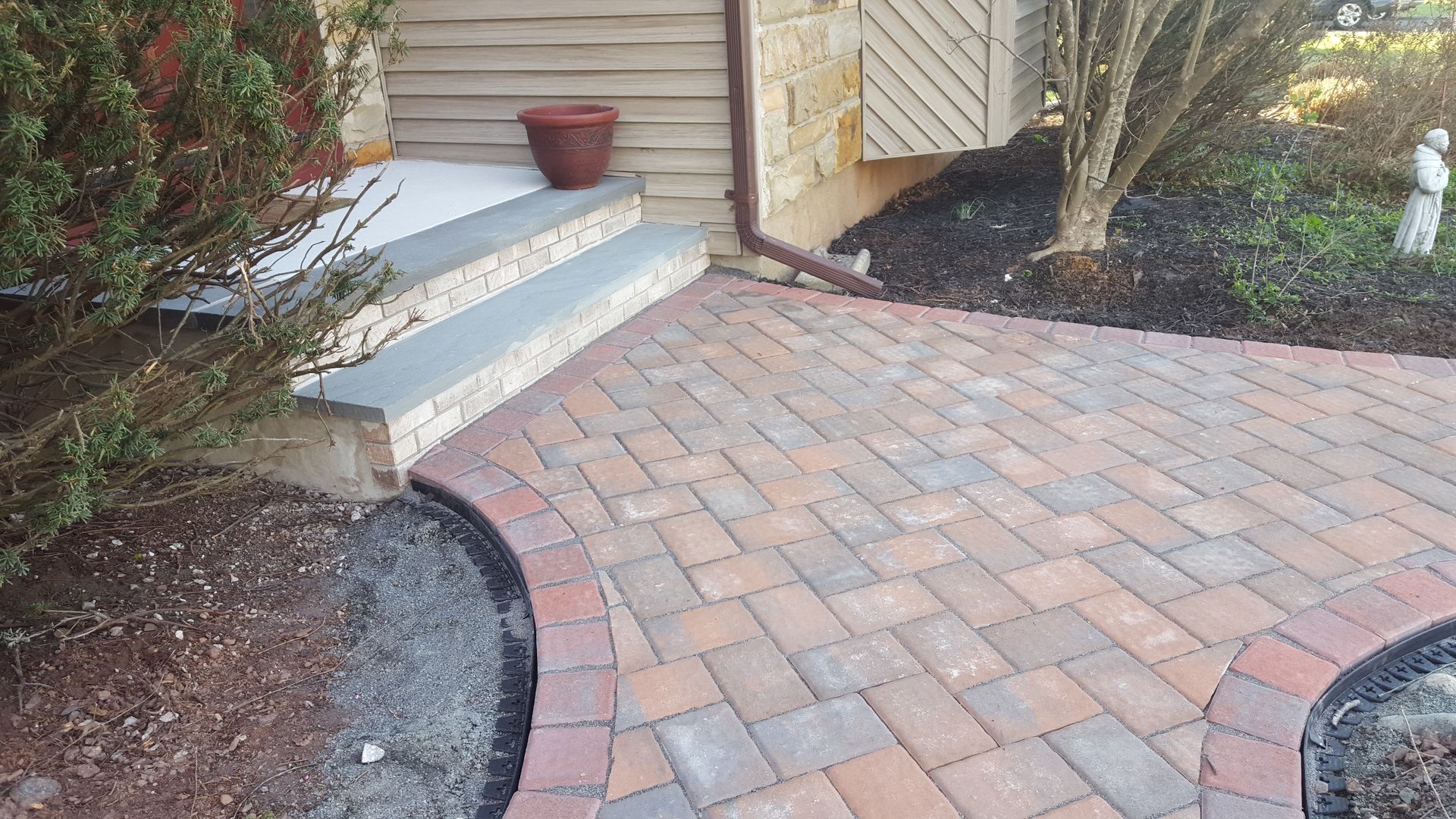Brick walkway leading to front steps and a house entrance with landscaped garden beds