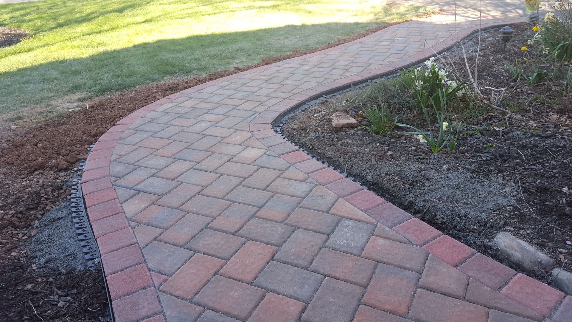 Curved brick garden path bordered by soil and grass in a landscaped yard