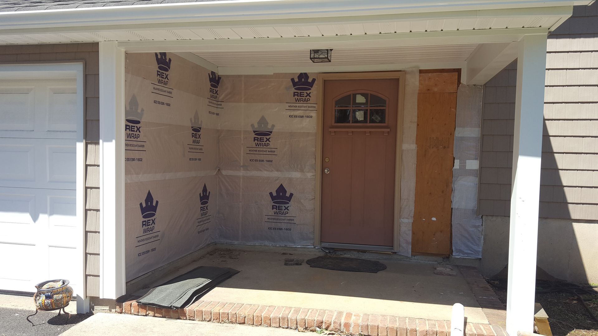 House porch under construction with wrapped walls, white columns, and a brown front door