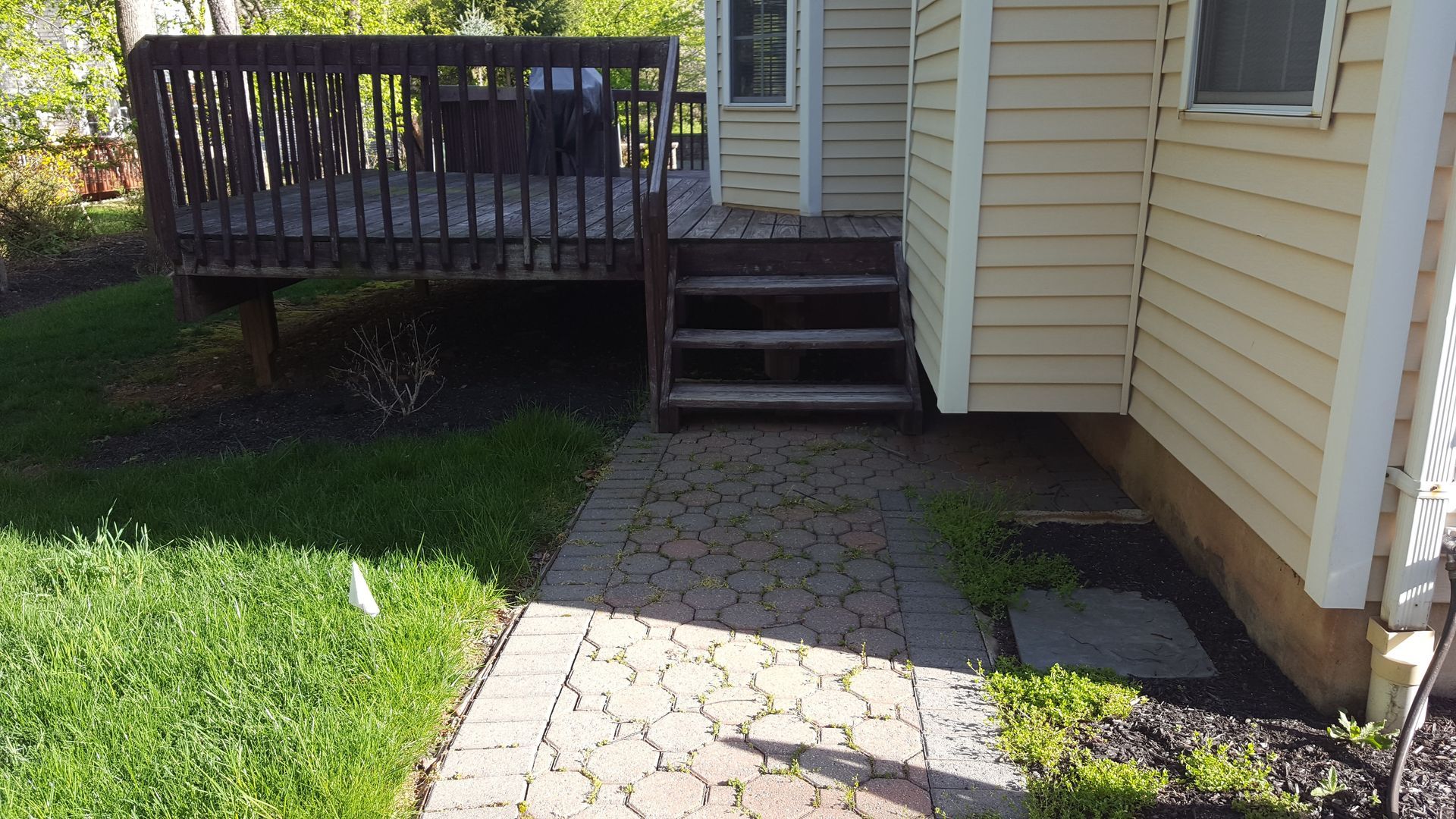 Backyard patio with stone path, wooden deck steps, and beige house siding