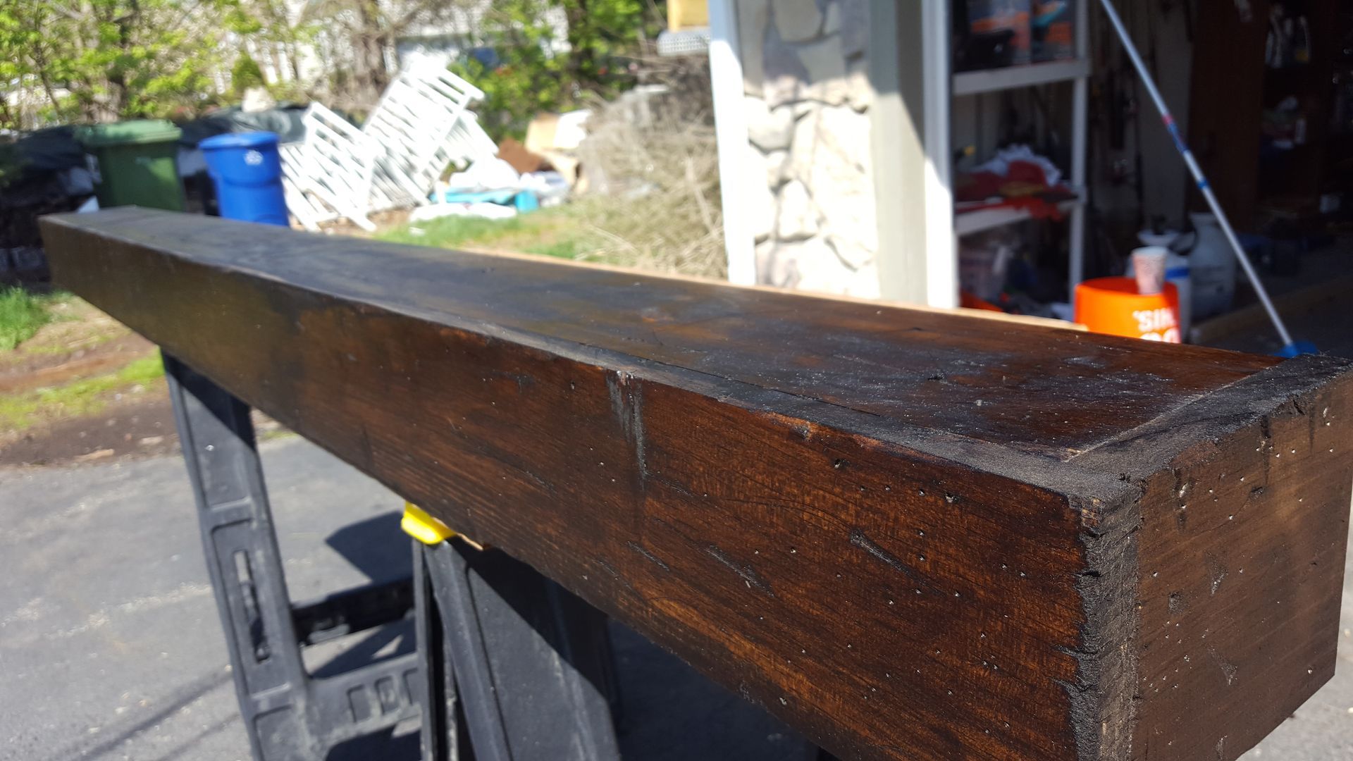 Close-up of a dark wooden beam on a workbench in an outdoor garage area.