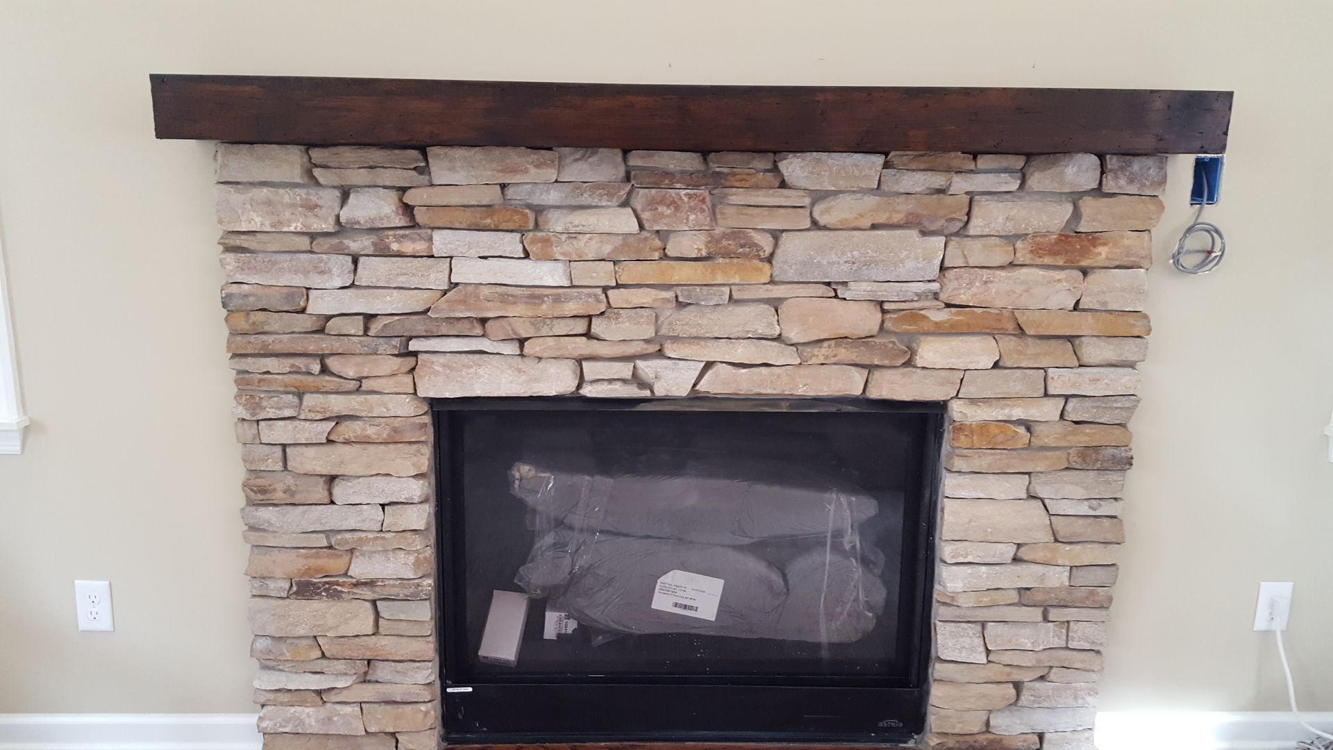 Stone fireplace with dark wood mantel and black firebox in a light-colored room