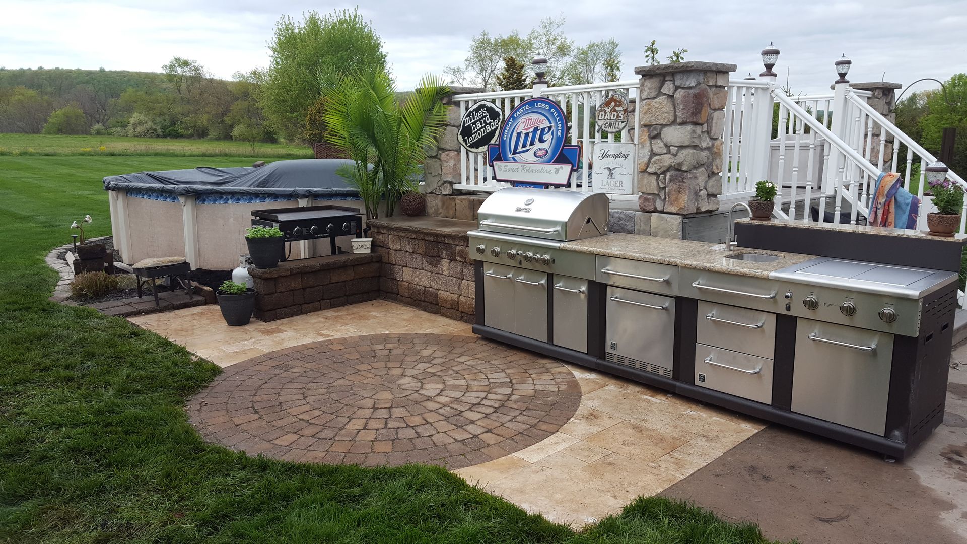 Outdoor patio with built-in grill, covered spa, stone fire pit, and metal storage cabinets.