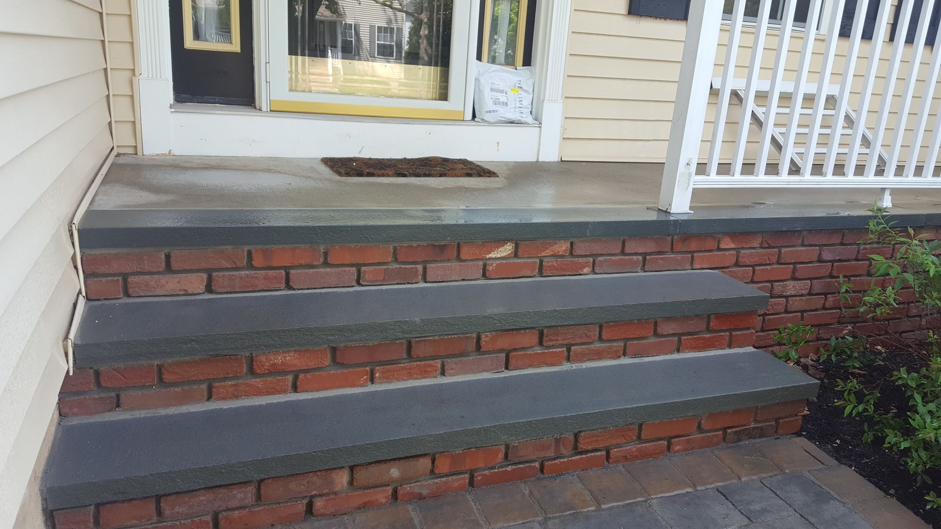 Front porch with brick steps, gray stair treads, white railing, and a door with a welcome mat