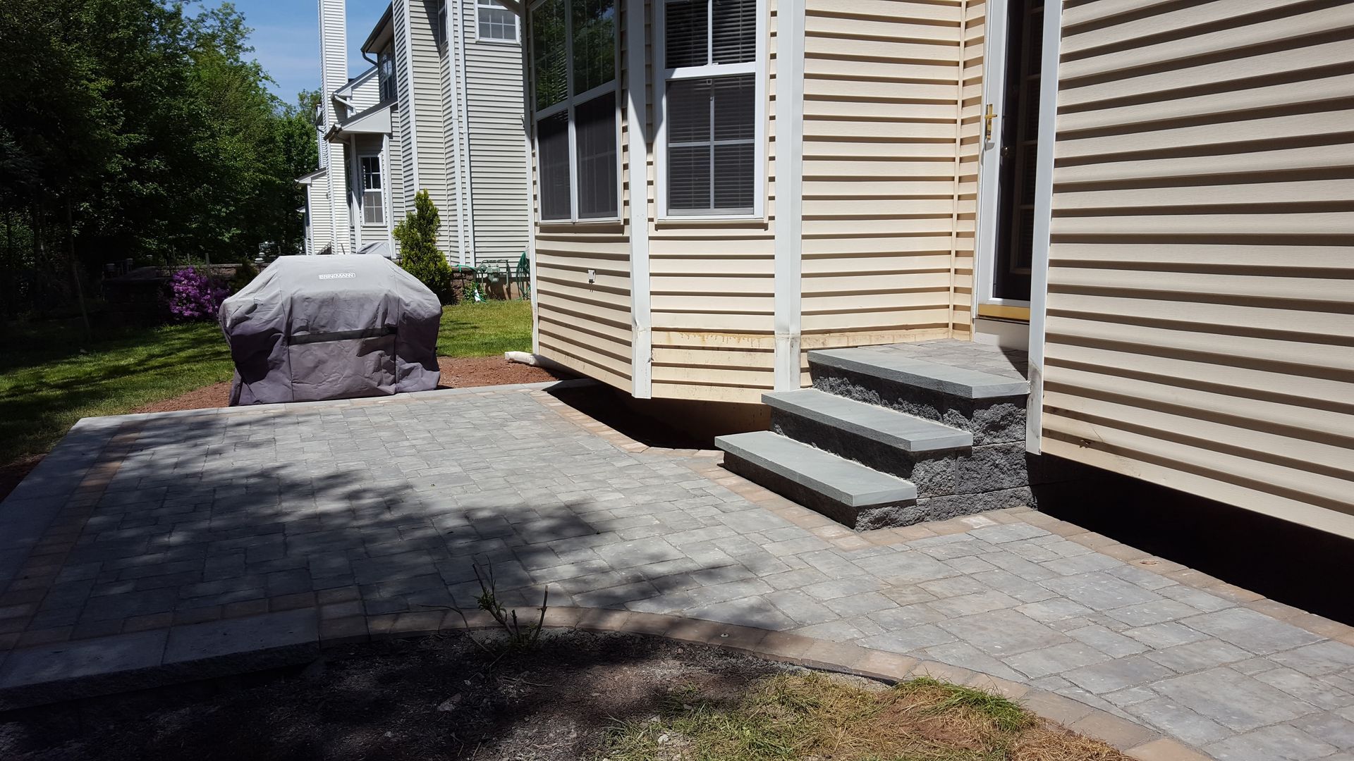Person bending over a paved walkway beside a beige house with steps and siding.