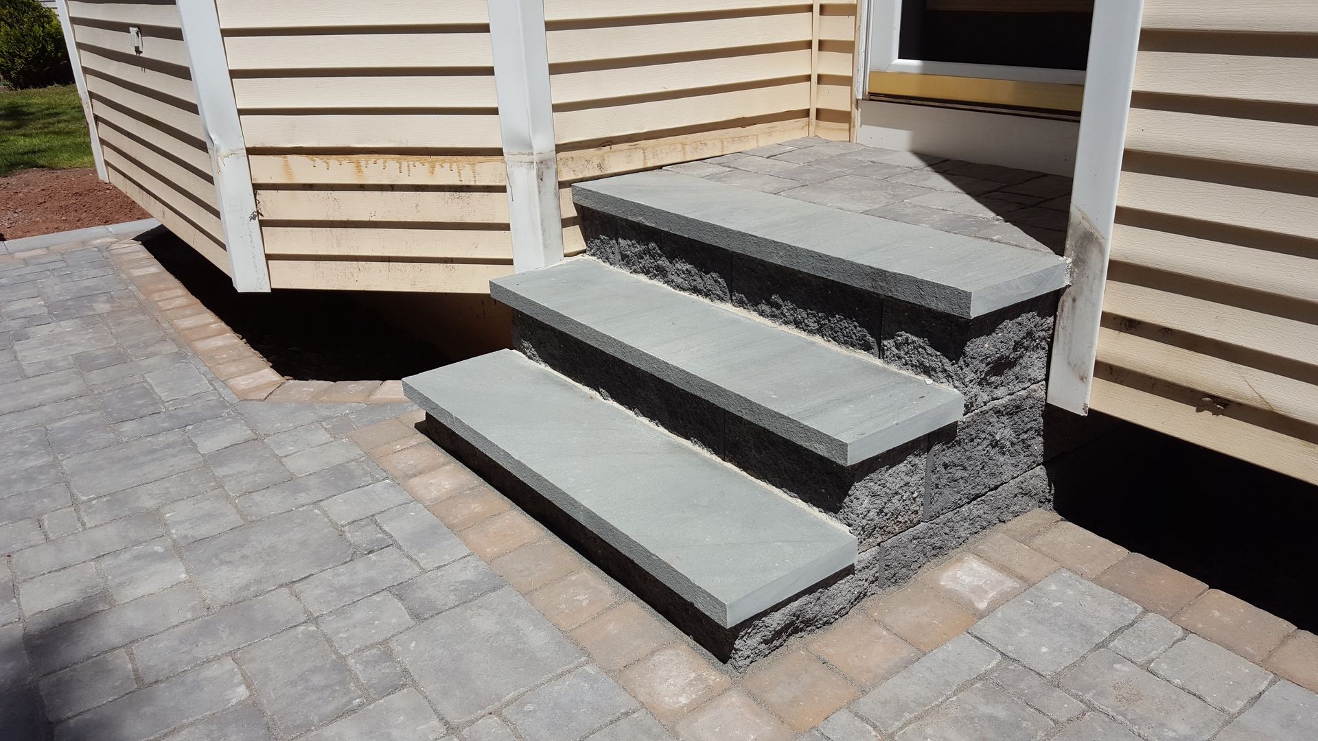 Three gray concrete steps leading to a raised doorway beside a paved patio