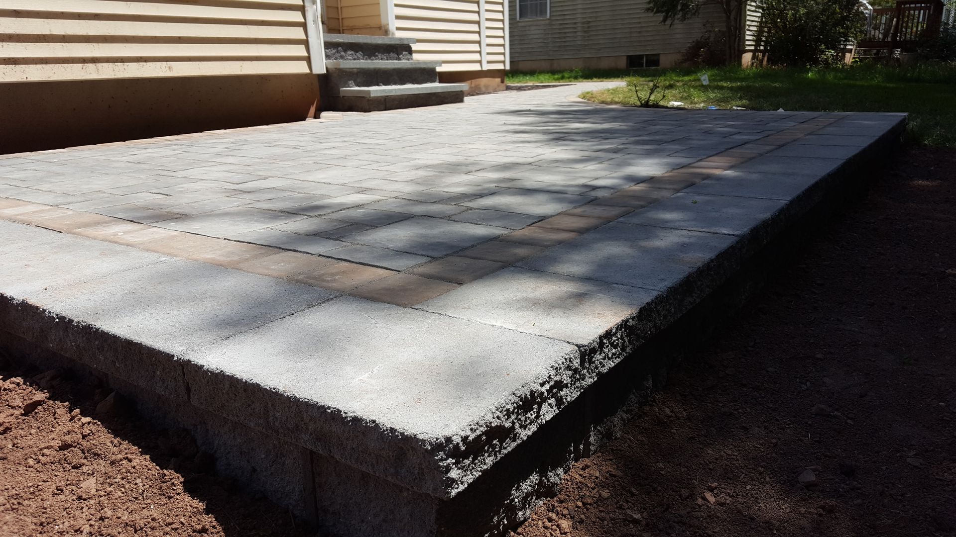 Concrete patio slab beside a house, with a raised edge and steps in the background