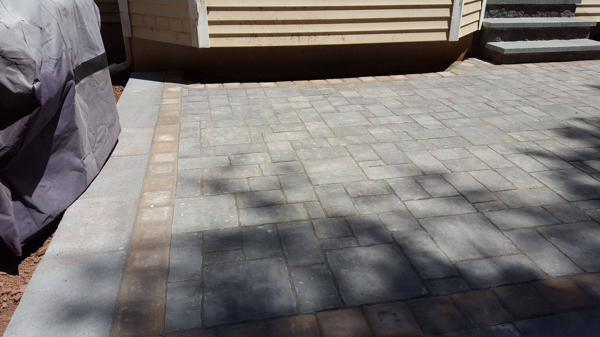 Stone-paved courtyard beside a wooden building, with sunlight and shadows across the ground.