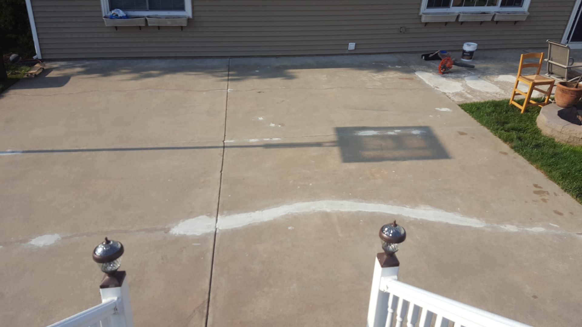 Concrete patio with white chalk lines and a small rectangular patch near a house exterior, viewed from steps.