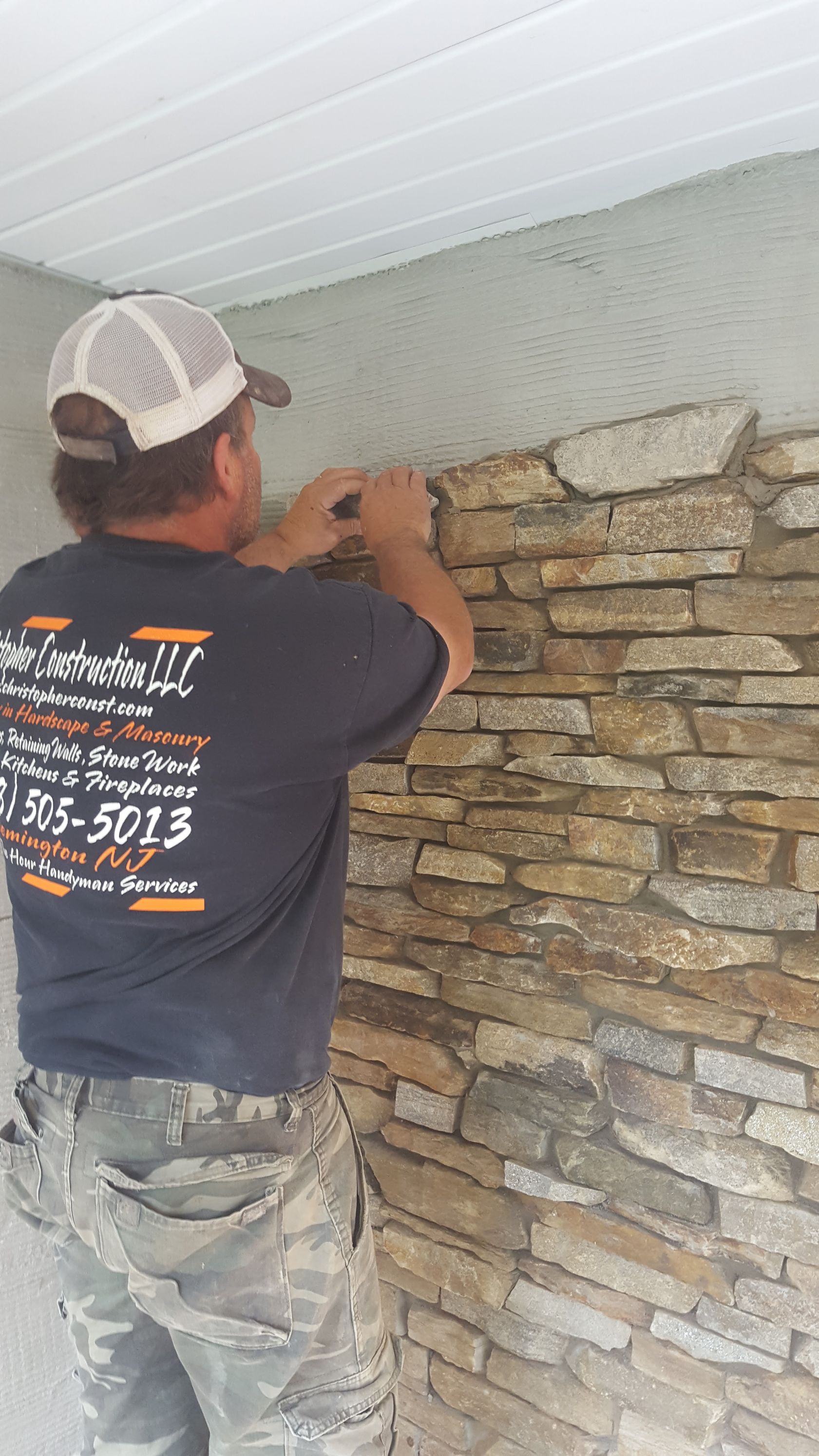 Worker installing stone veneer on an exterior wall under a white ceiling