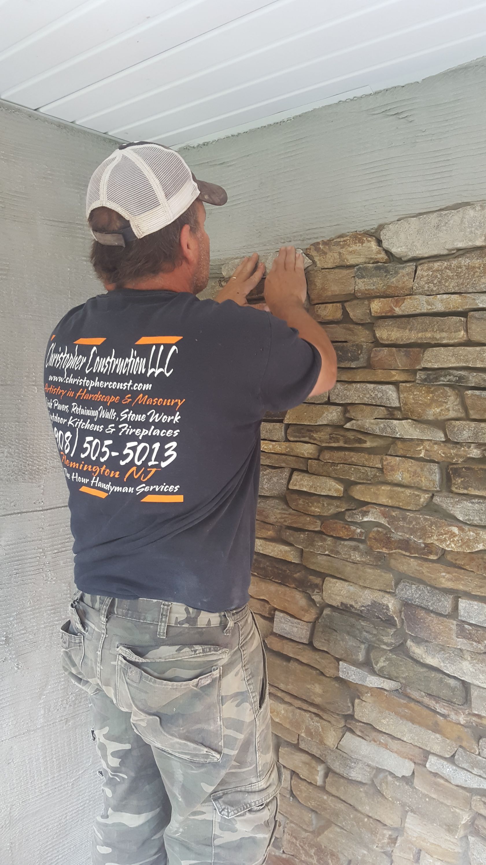 Worker installing stacked stone wall under a white ceiling inside a room.