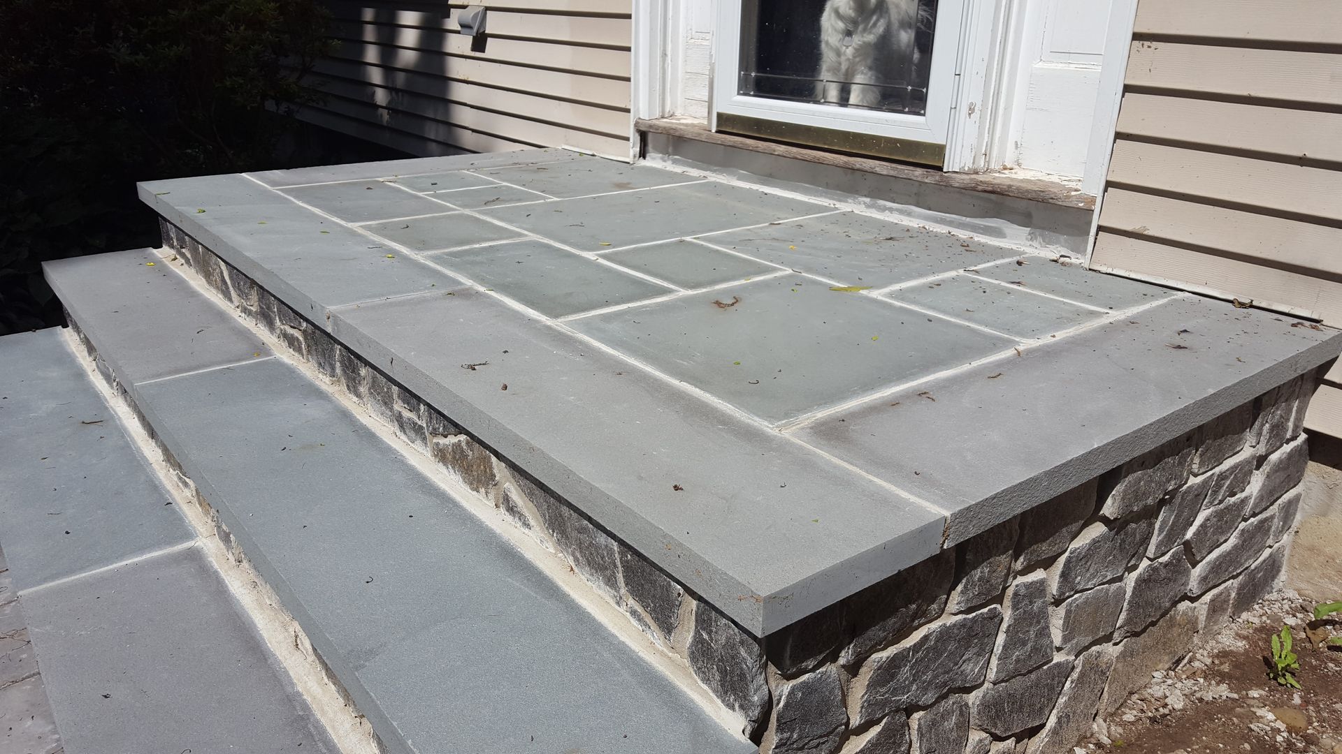 Concrete front porch with stone sides and a tiled walkway leading to a door