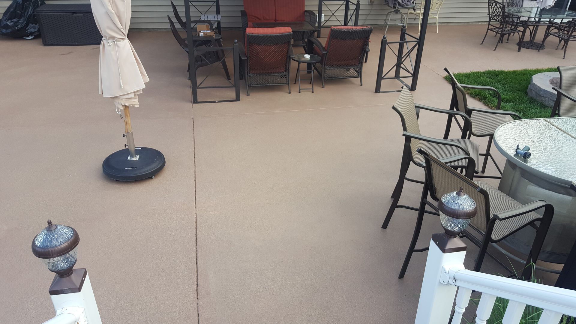 Outdoor patio with glass tables, black chairs, and a closed umbrella on a beige surface