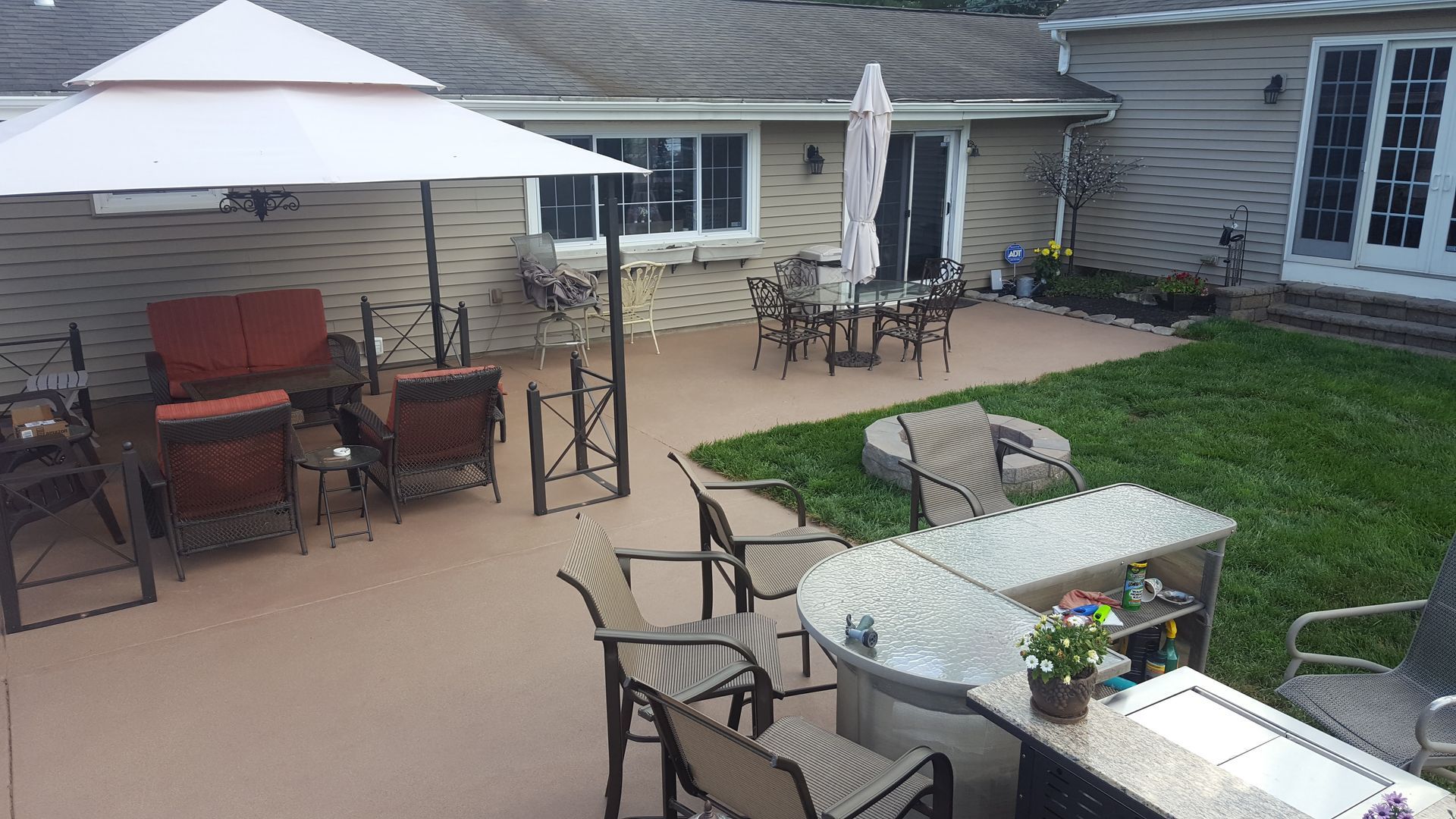 Backyard patio with umbrella-covered seating, grill, table, and a small lawn beside a house