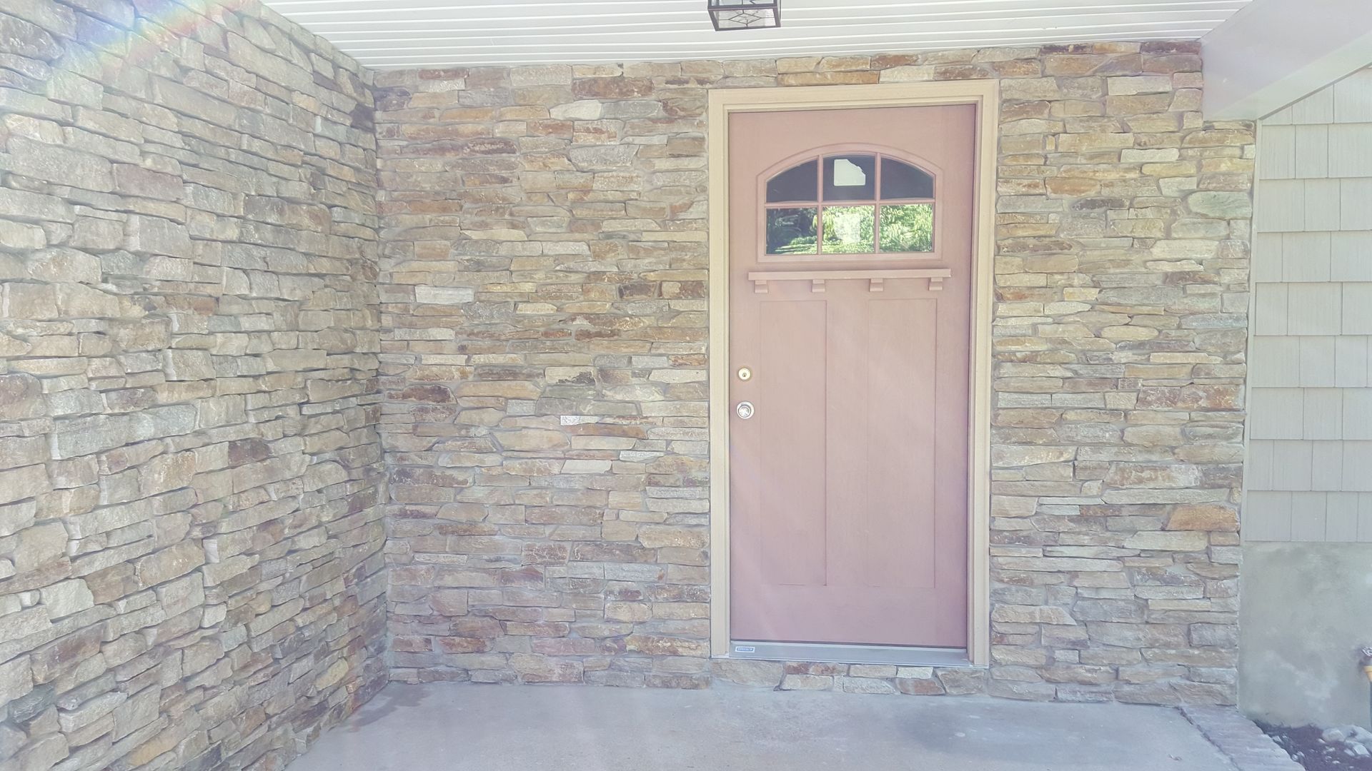 Stone entryway with a tan door and small arched window at the center.