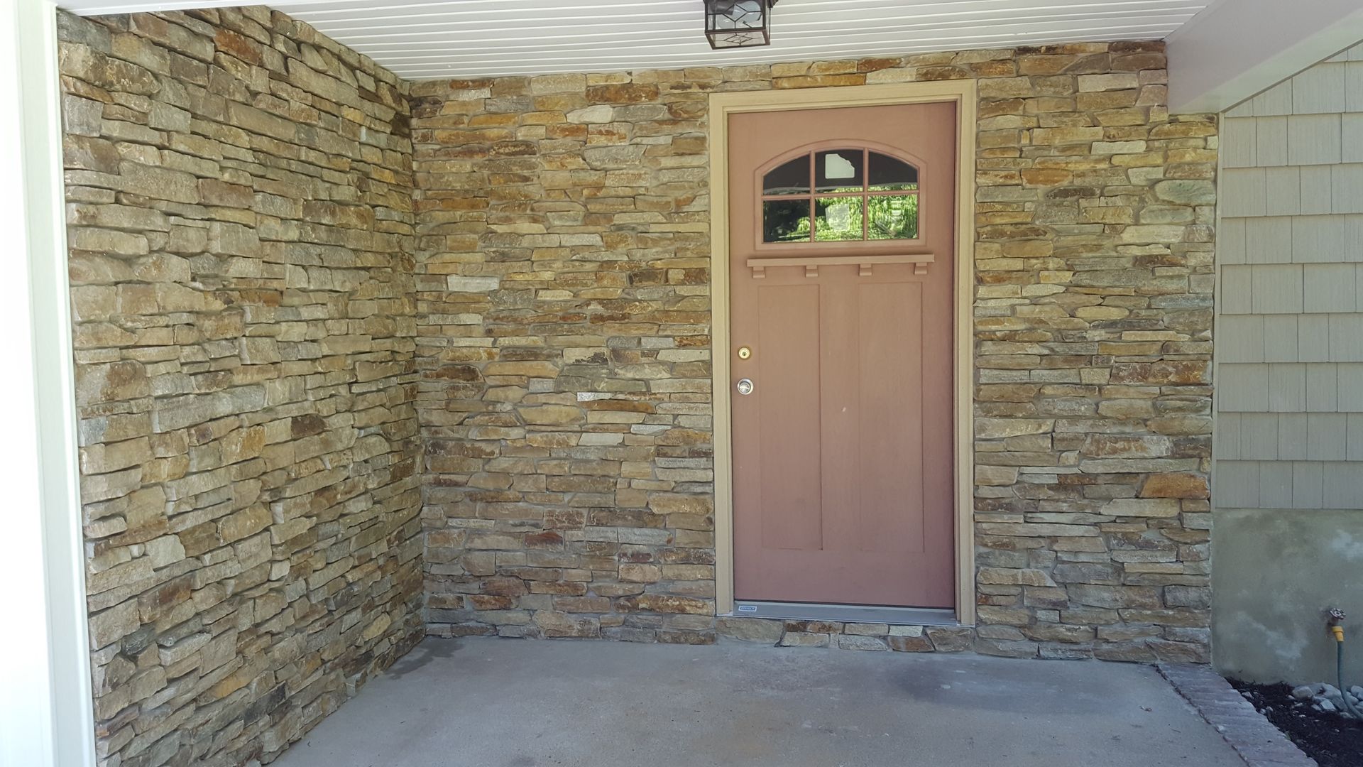 Covered porch with tan stone walls and a brown door centered at the back.