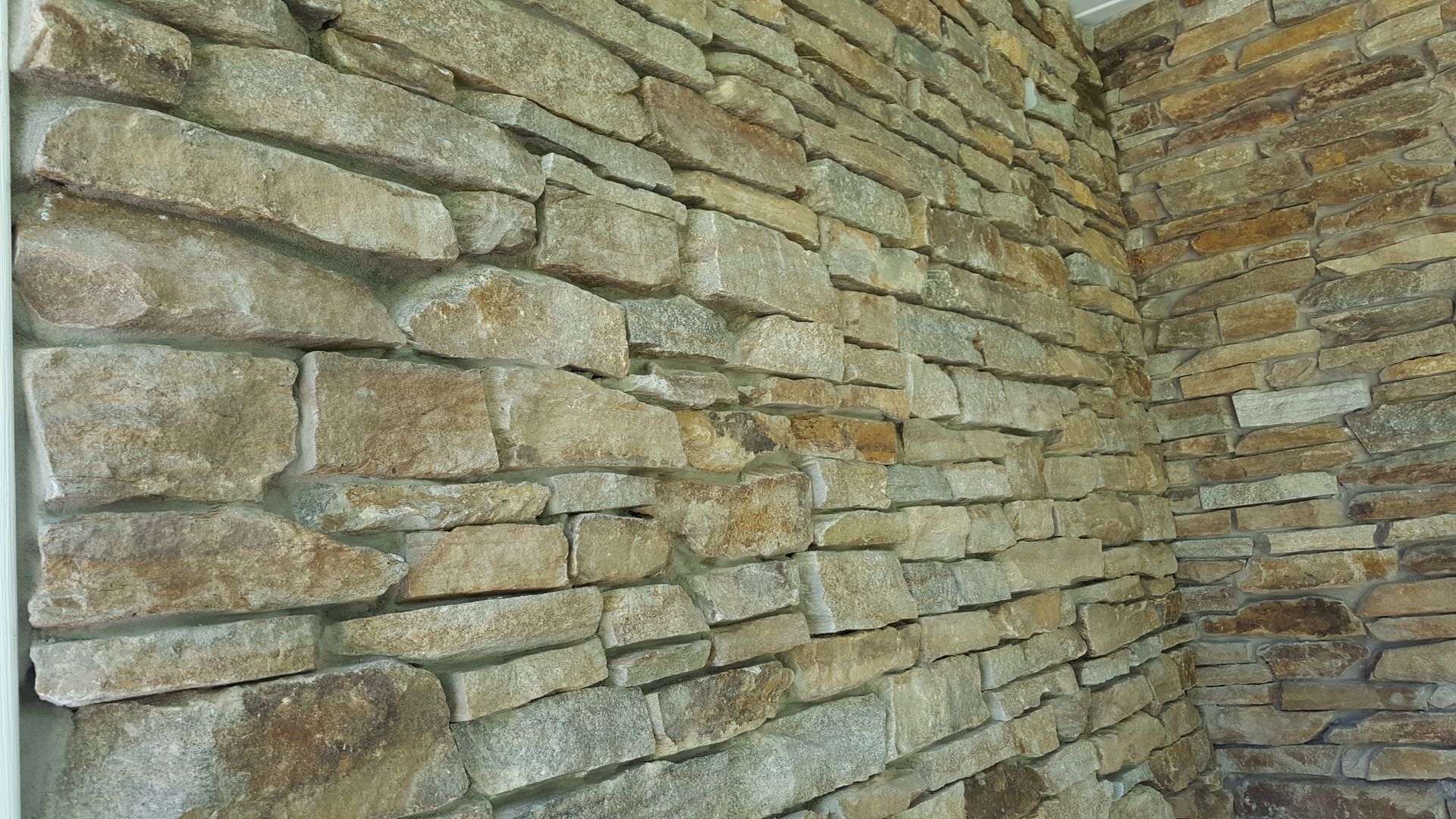 Close-up of a textured stone wall with layered tan and gray stones.