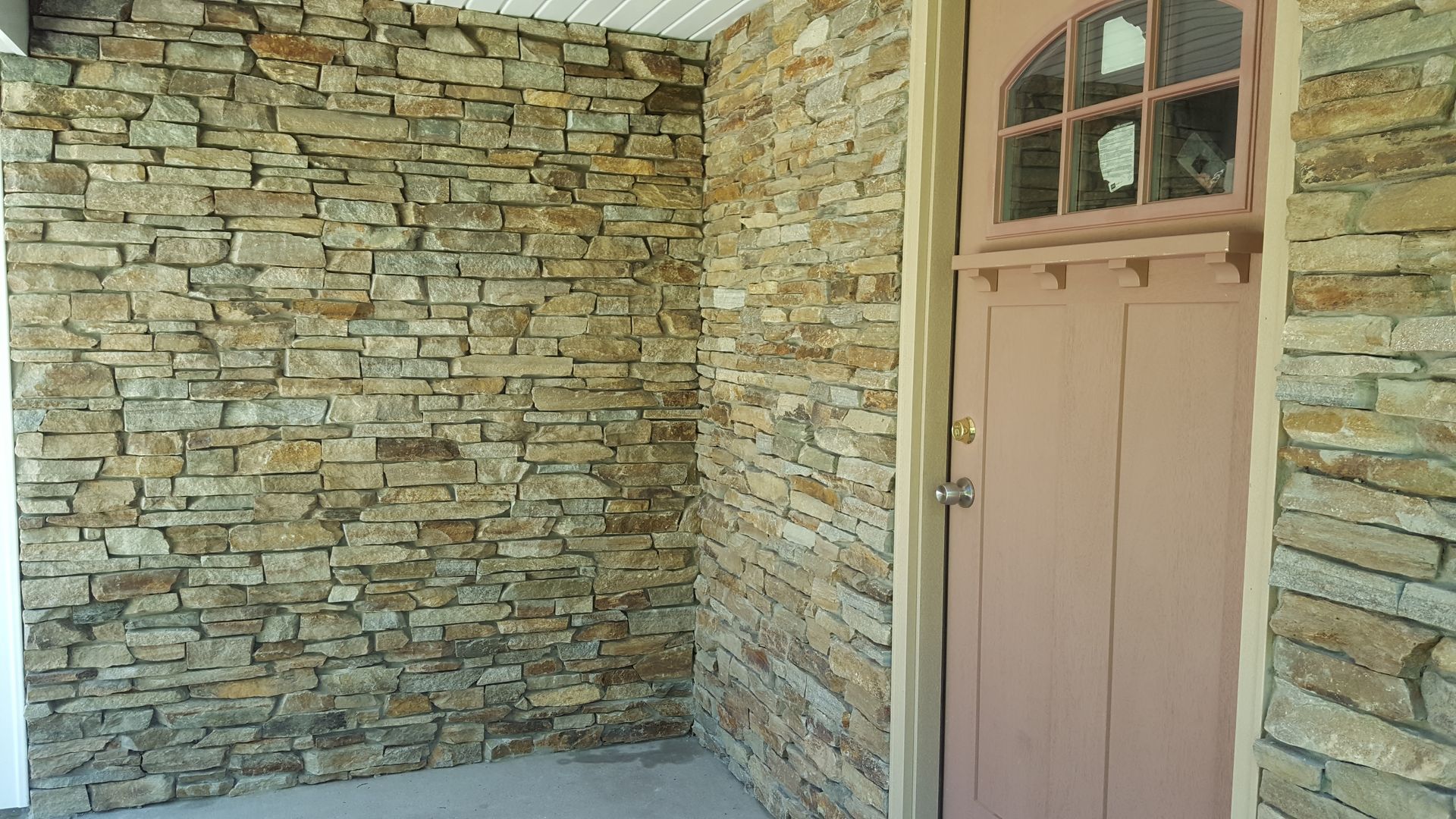Stone exterior wall and beige door with a small arched window above it.