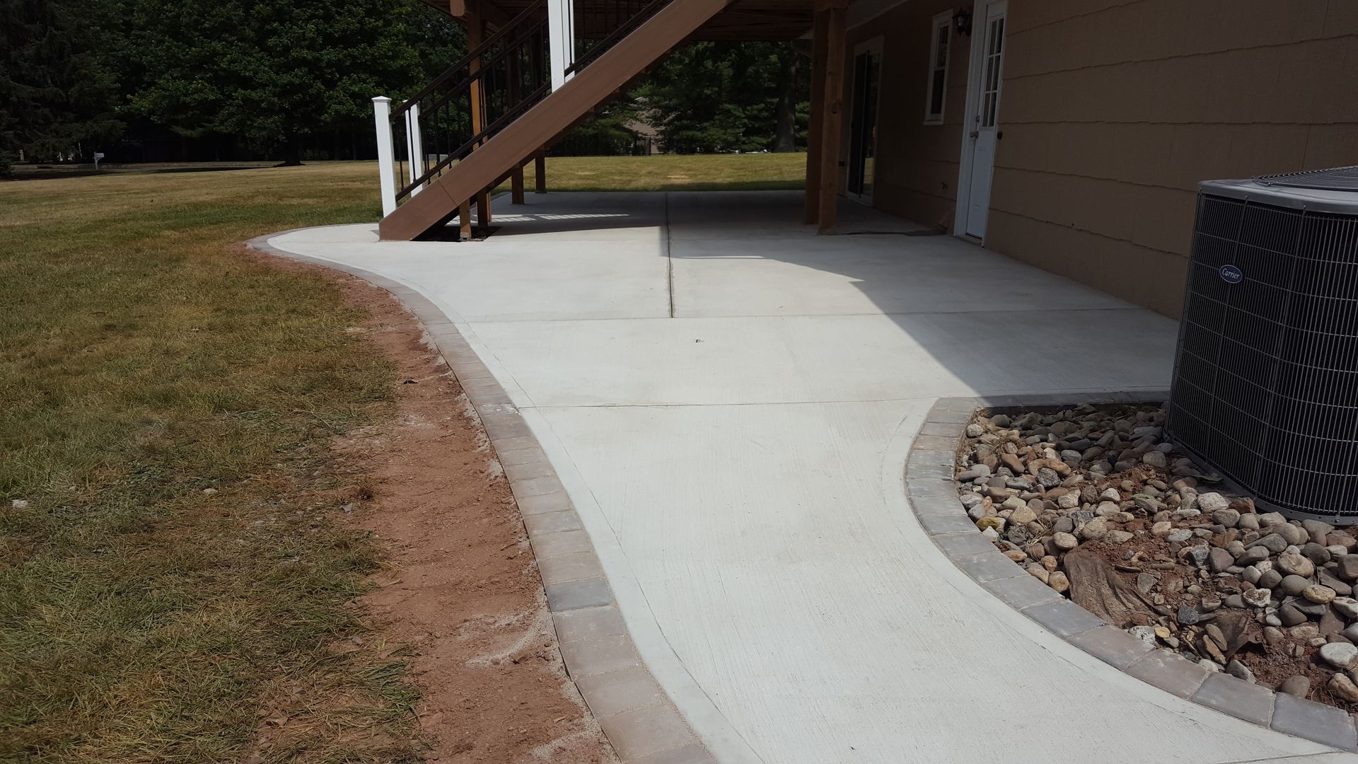 Curved concrete walkway beside a building, with a raised stairway and landscaped rock bed.