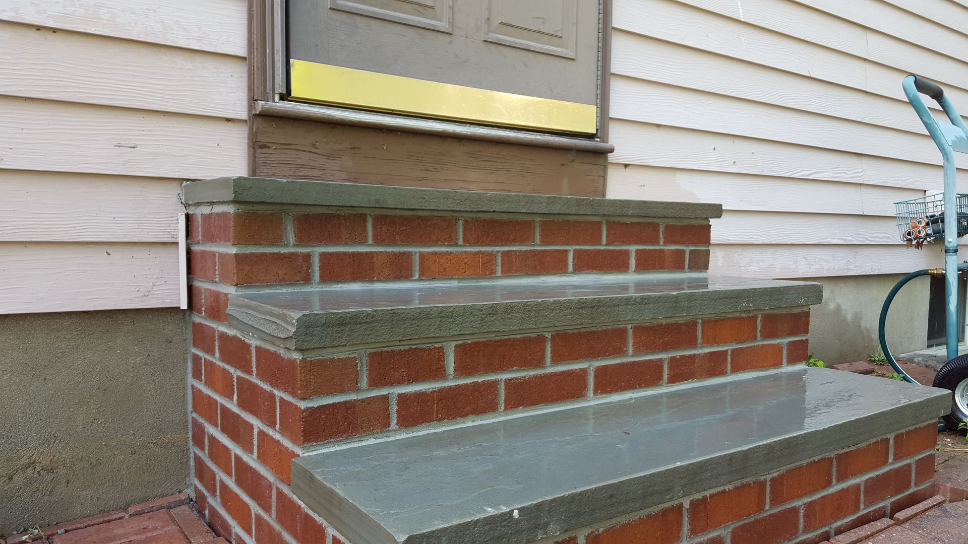 Red brick front steps with gray concrete landing leading to a house doorway