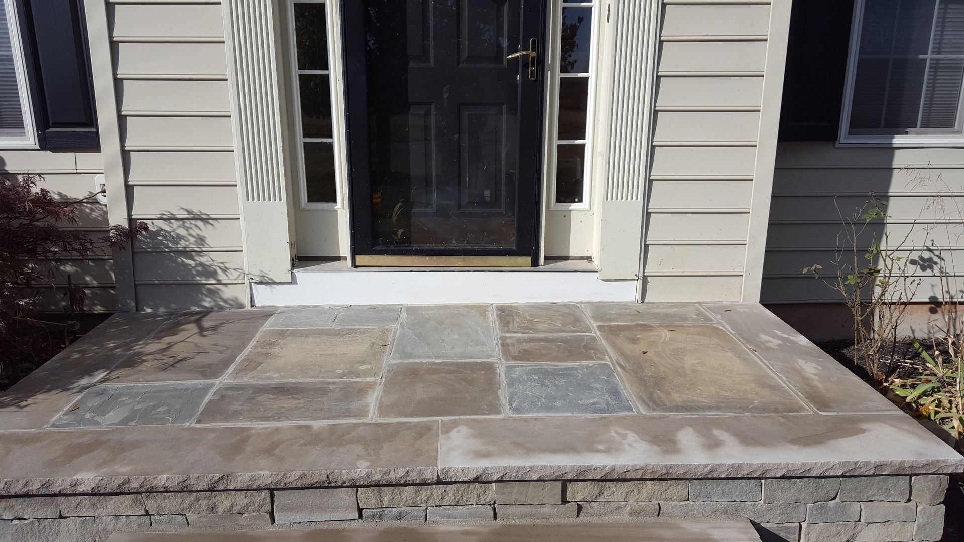 Stone front porch with steps leading to a dark doorway and beige siding exterior