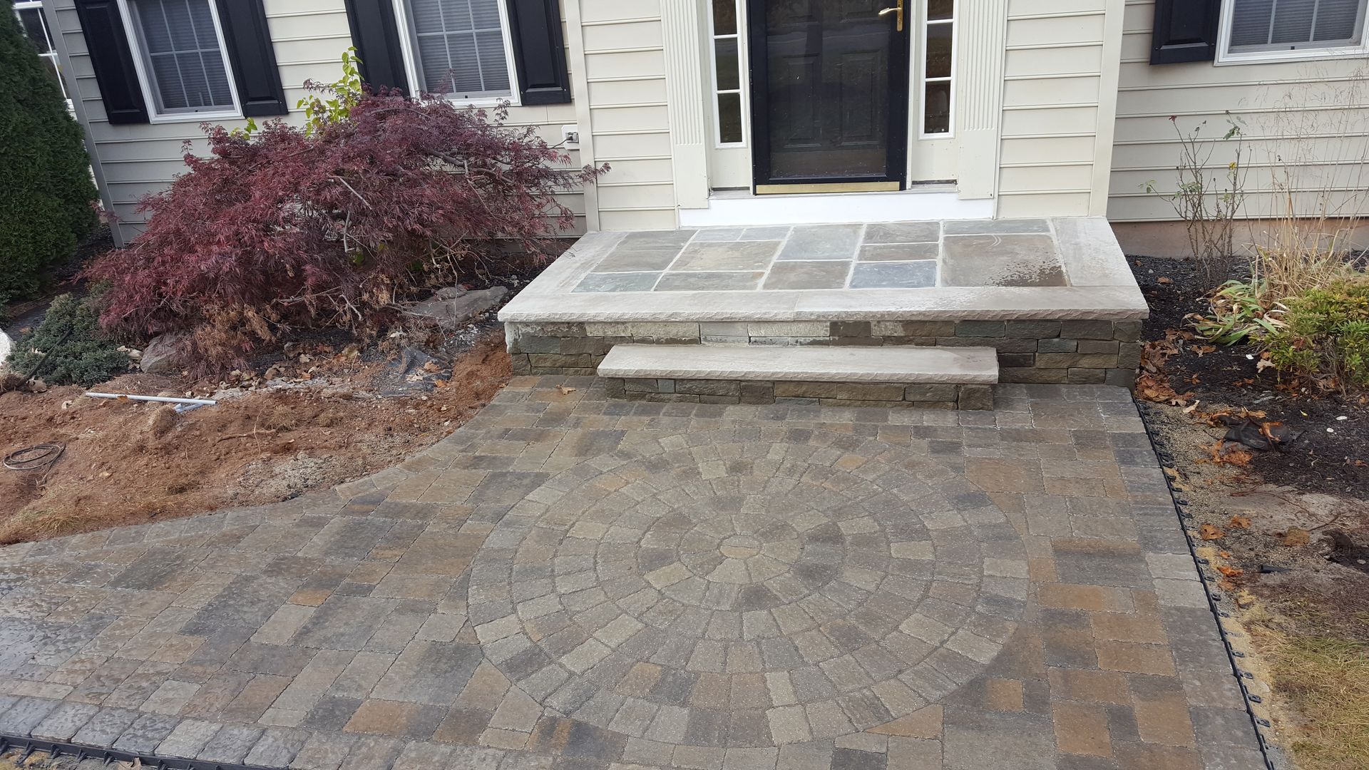 Brick paver walkway leading to a house entrance with stone steps and front shrubs