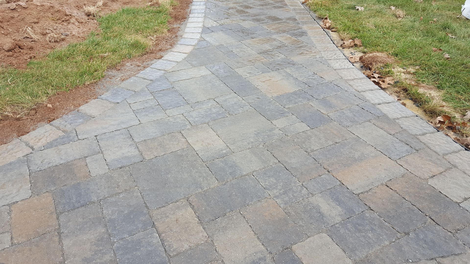 Curved stone-paver walkway bordered by grass and mulch outdoors