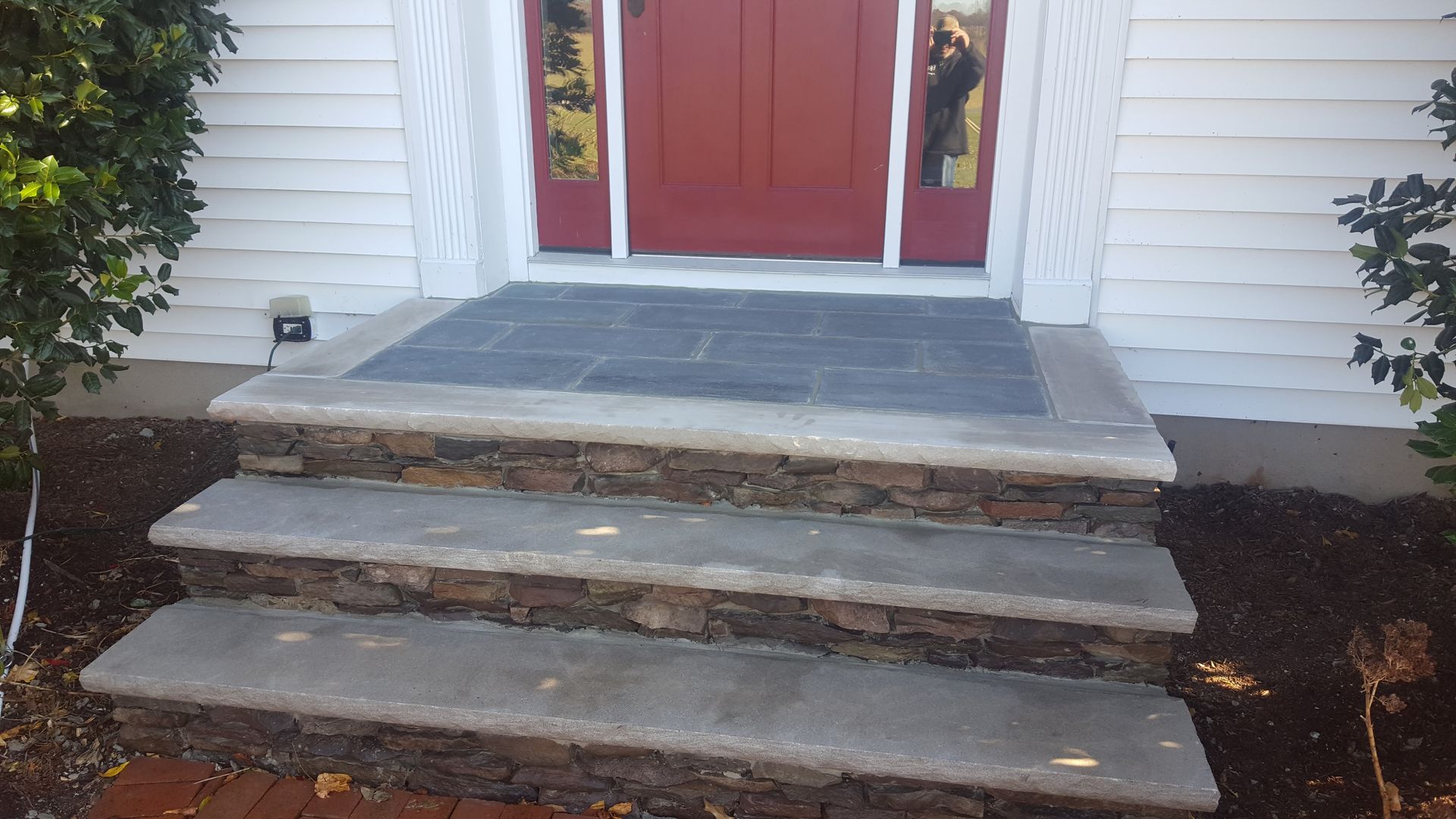 Front steps and red double doors with stone risers and white siding on either side