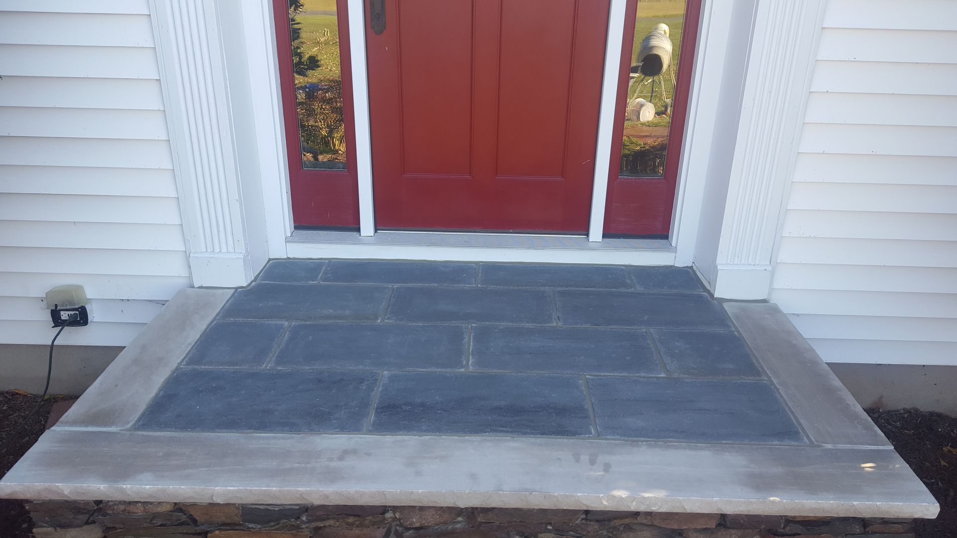 Front porch with a dark gray tiled landing leading to red double front doors.