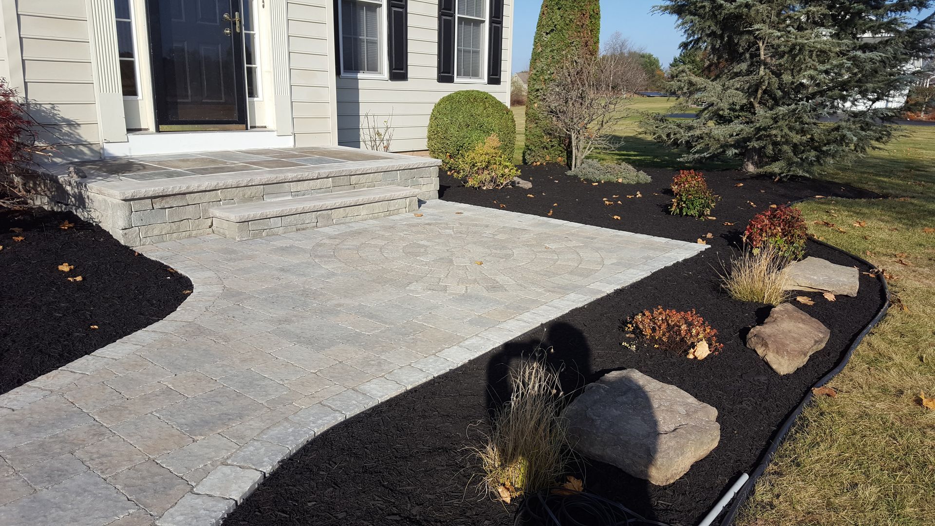Front walkway with gray pavers and black mulch landscaping leading to a house entrance