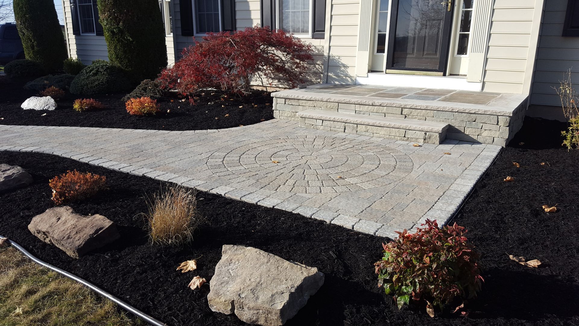 Front porch entrance with stone steps, black mulch, and red shrubs beside a white house
