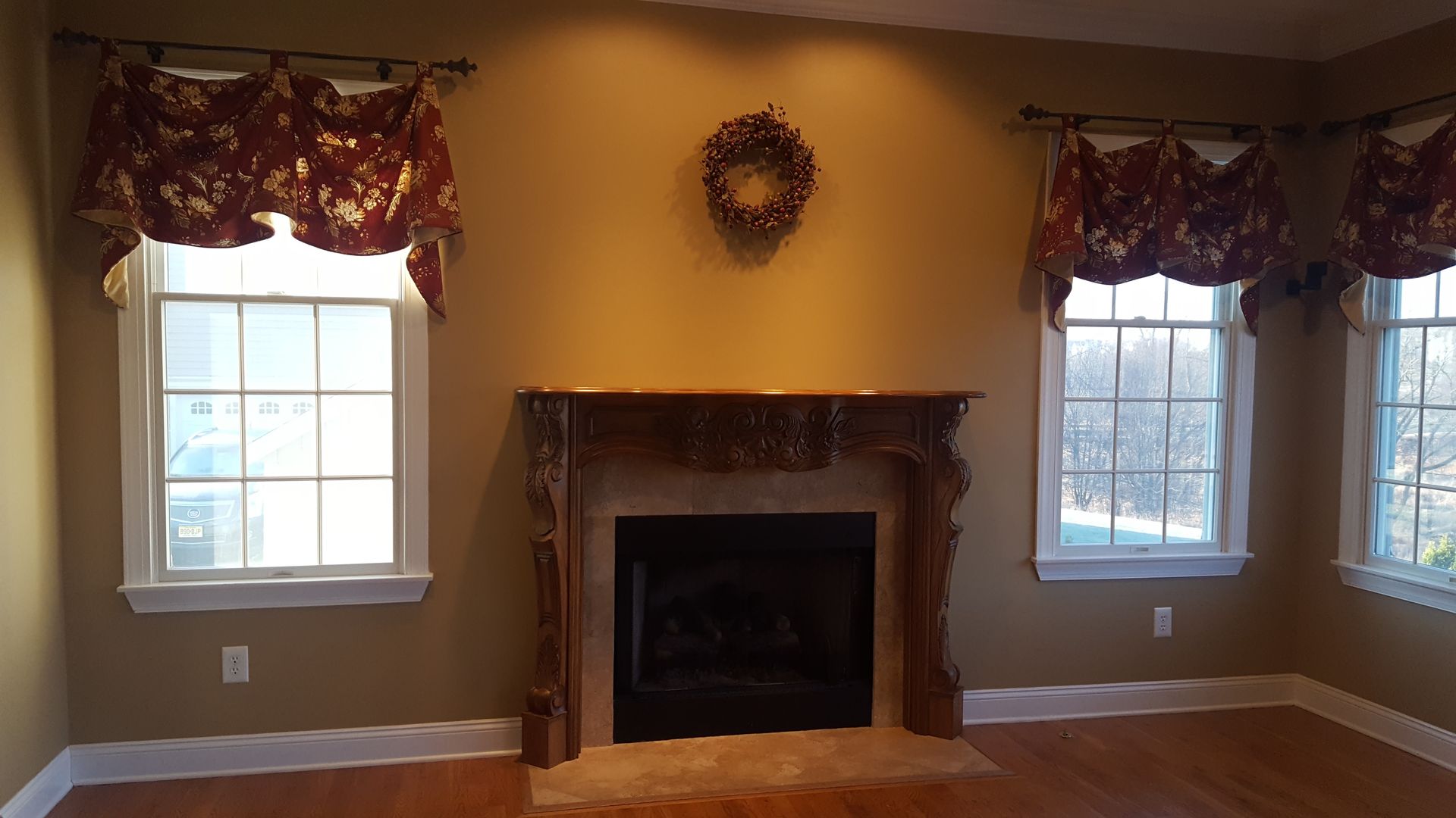 Living room with fireplace, two windows with red valances, tan walls, and hardwood floors