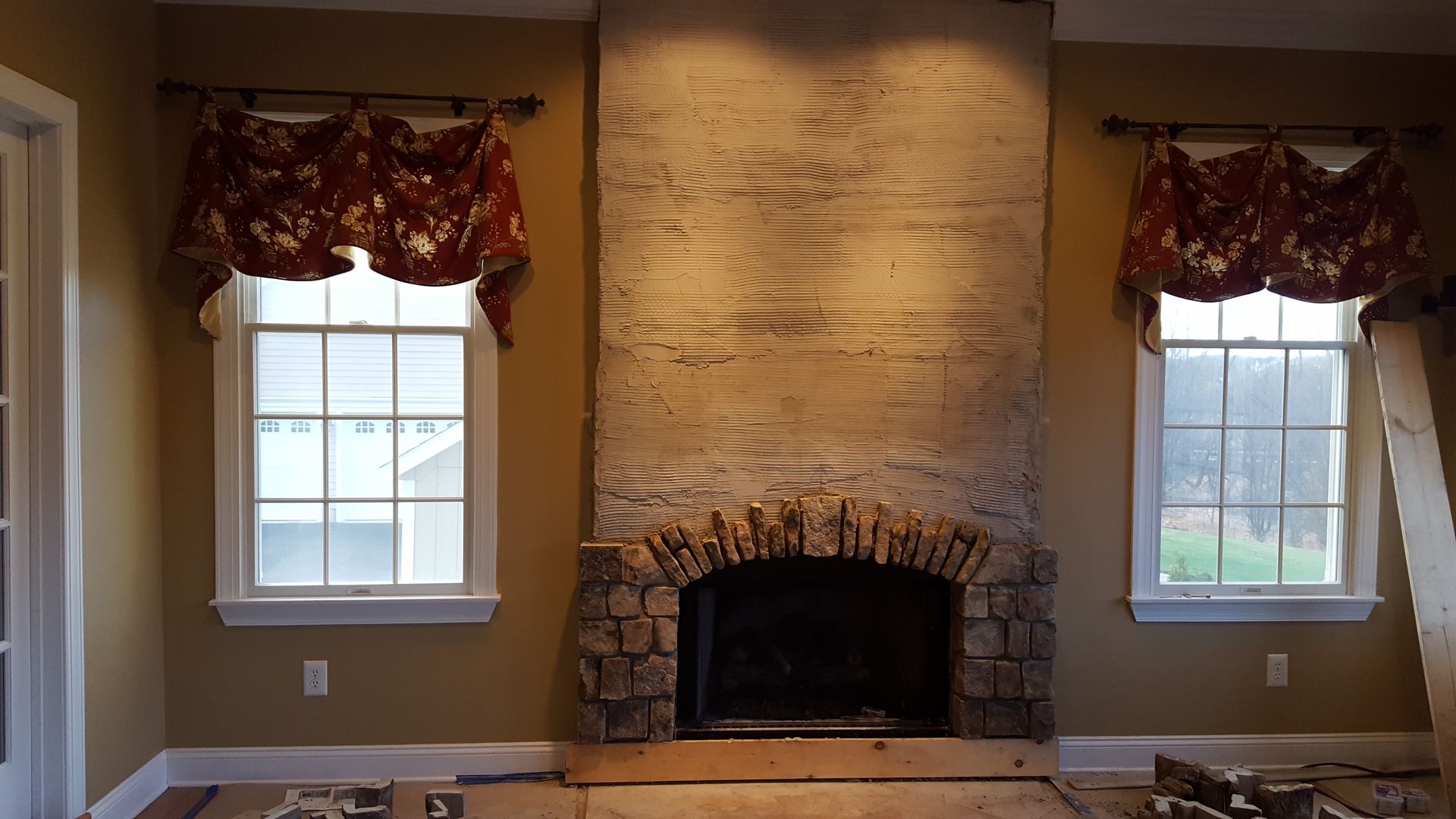 Living room fireplace with stone surround and two windows with red curtains