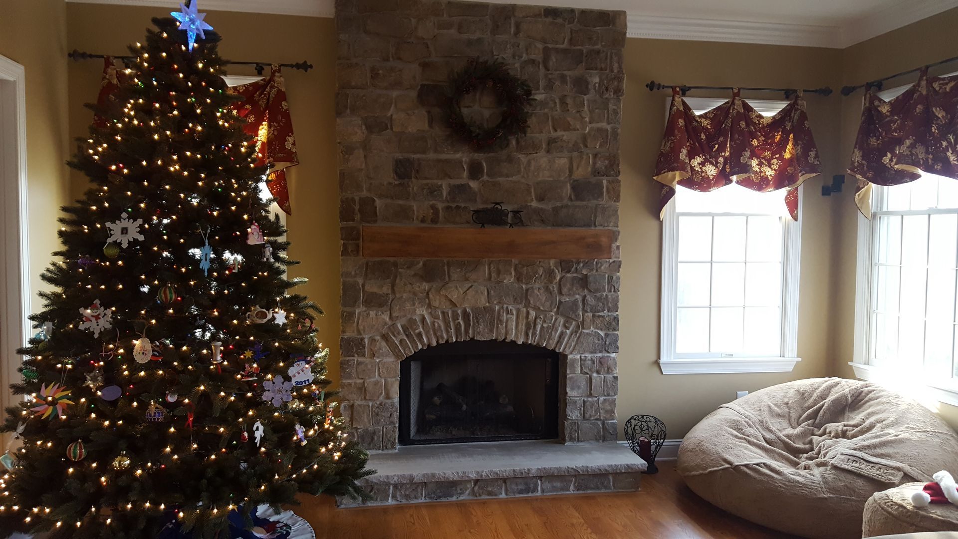 Living room with lit Christmas tree, stone fireplace, and bright window with beanbag chair