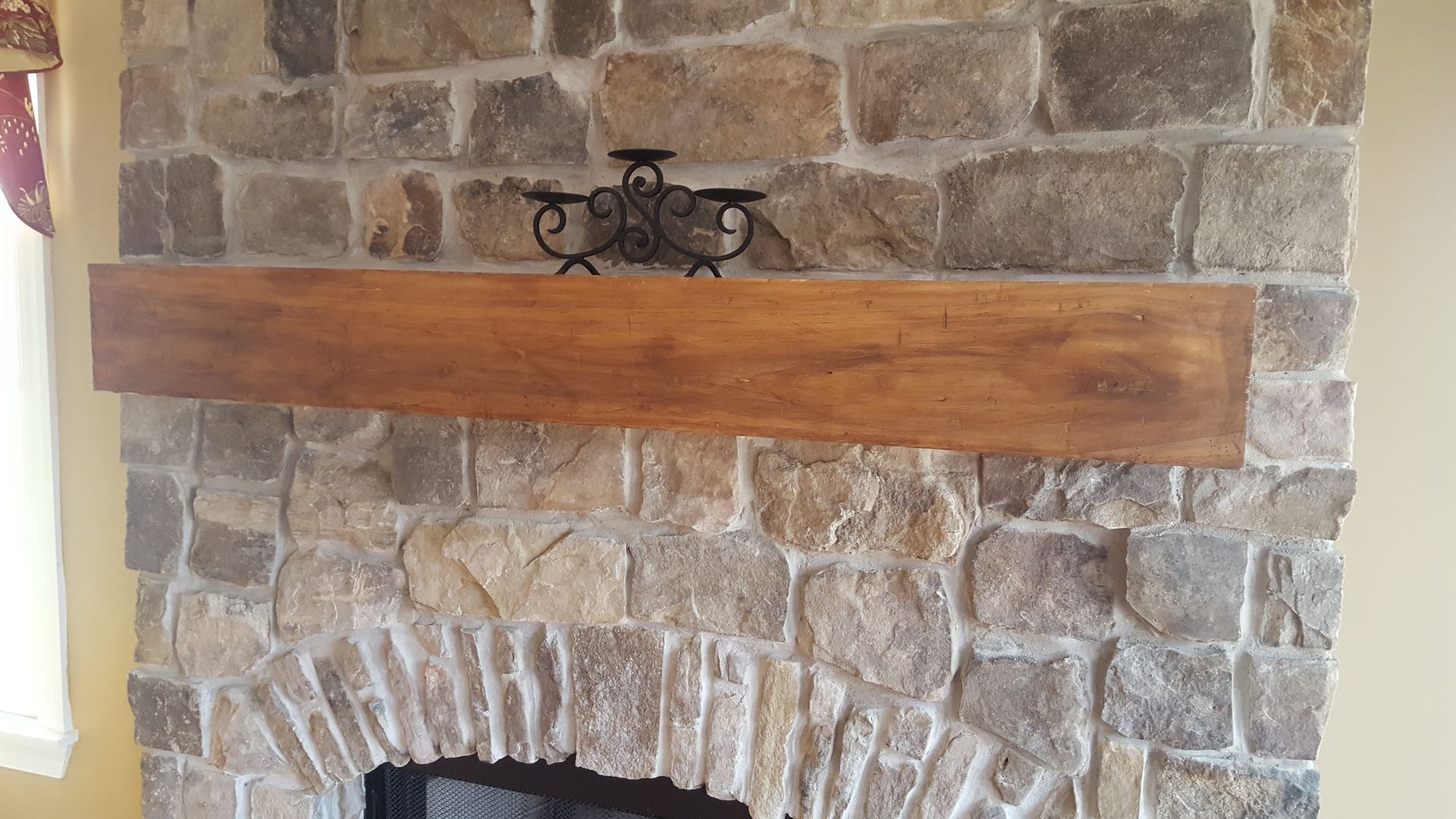 Stone fireplace with a long wooden mantel and a small wrought-iron decoration above it
