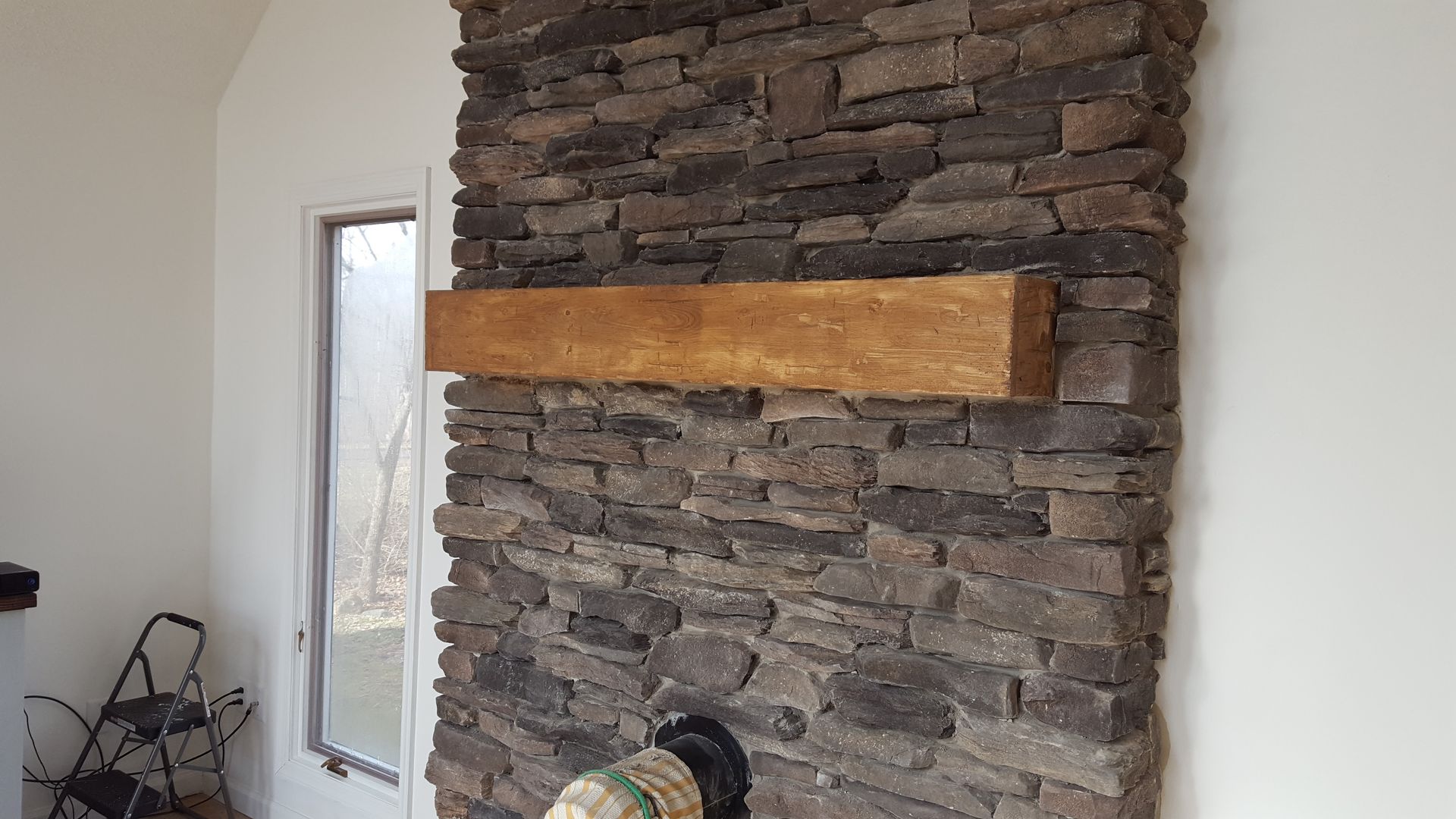 Stone fireplace with a long wooden mantel in a bright room