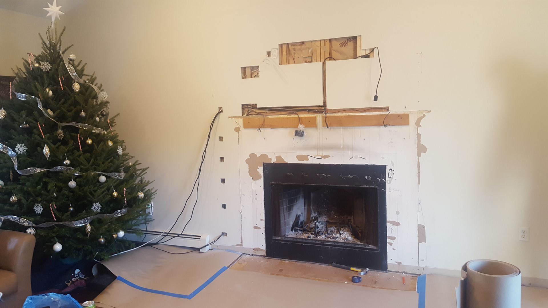 Christmas tree beside a white fireplace with stockings, lights, and a TV above the mantel in a living room