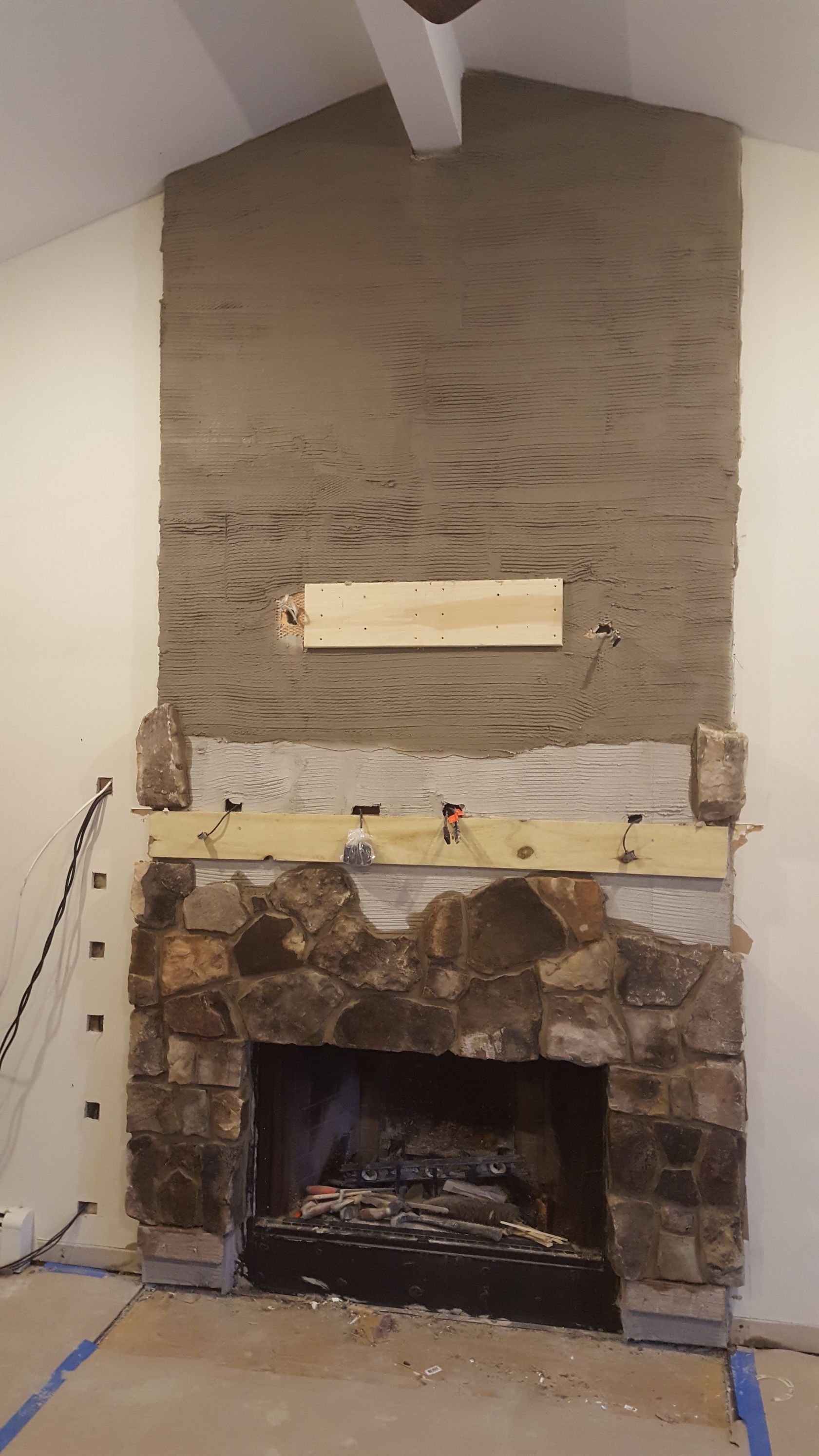 Stone fireplace with a rough plaster chimney wall and a white mantel in a room with a high ceiling