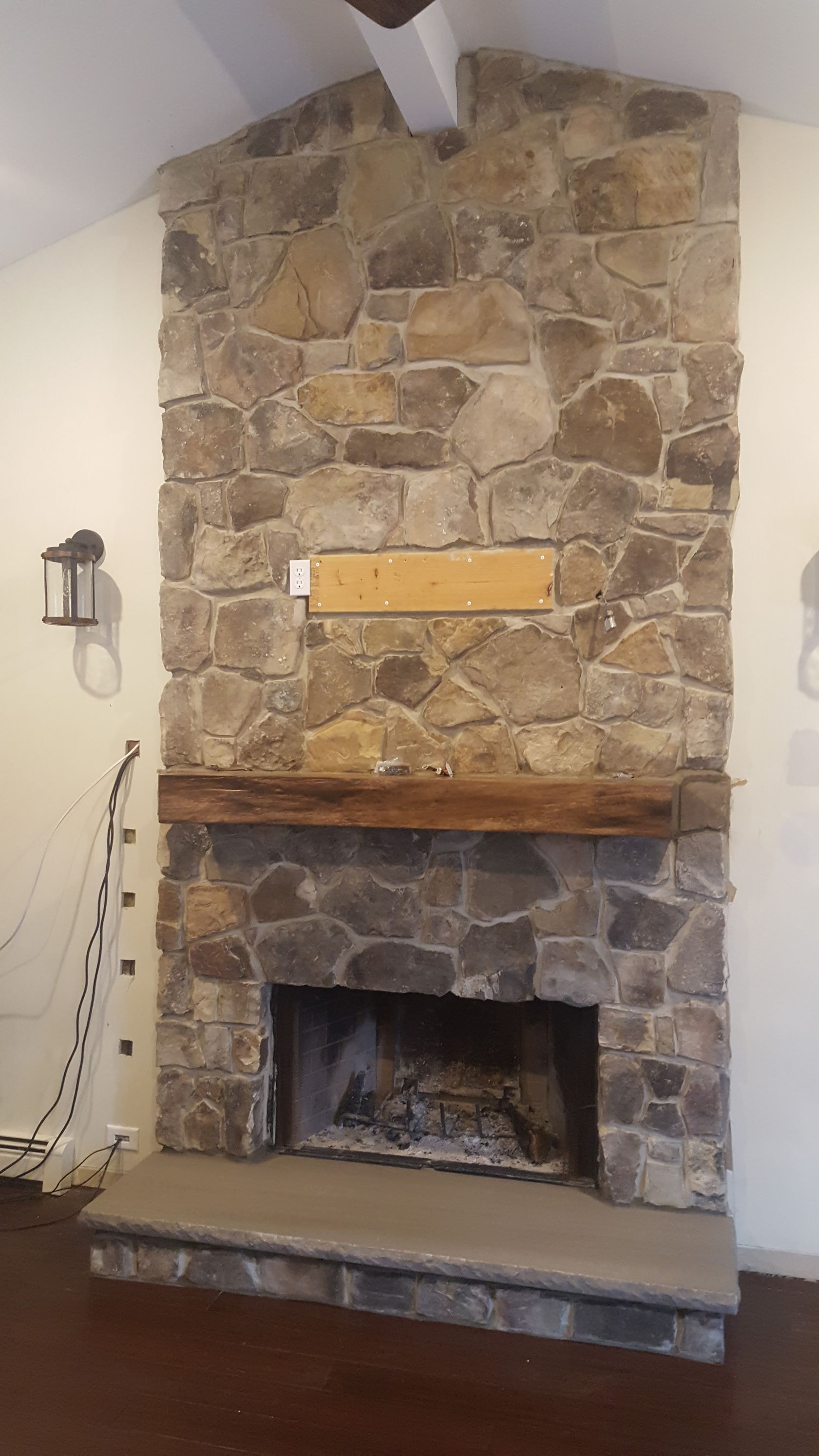 Stone fireplace with wooden mantel and rough stone chimney in a room with white walls.