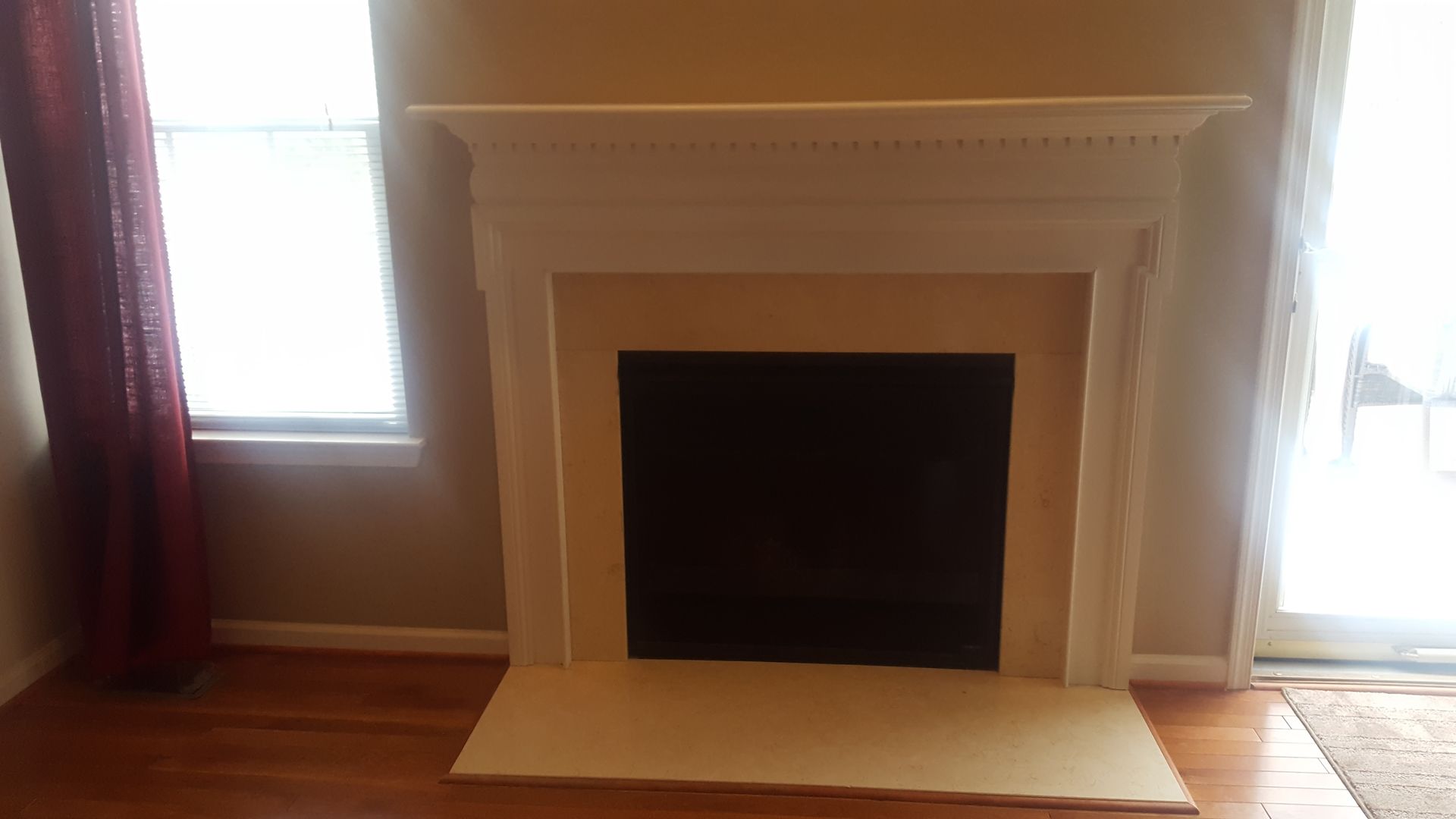 Empty fireplace with cream mantel between two bright windows in a hardwood-floored room