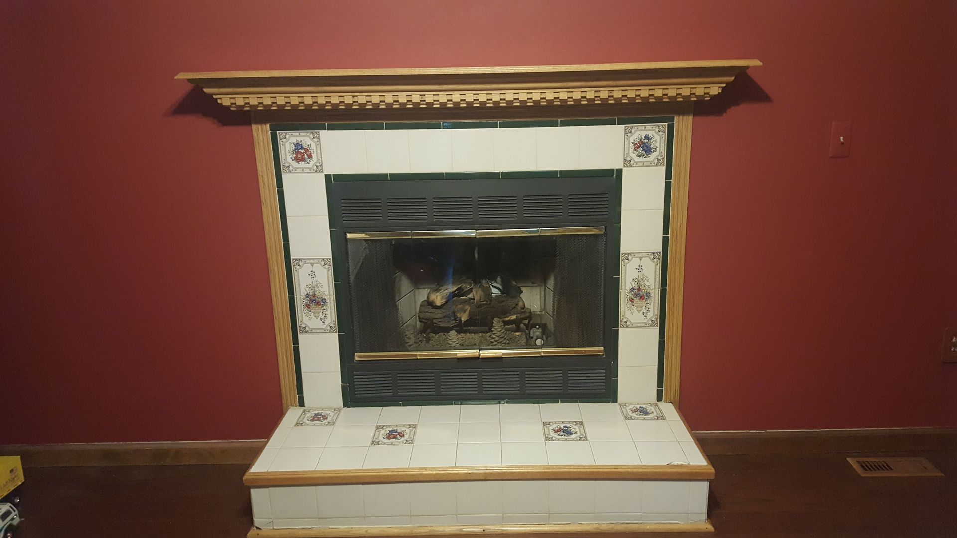 White ornate fireplace mantel against a red wall with a dark firebox opening.