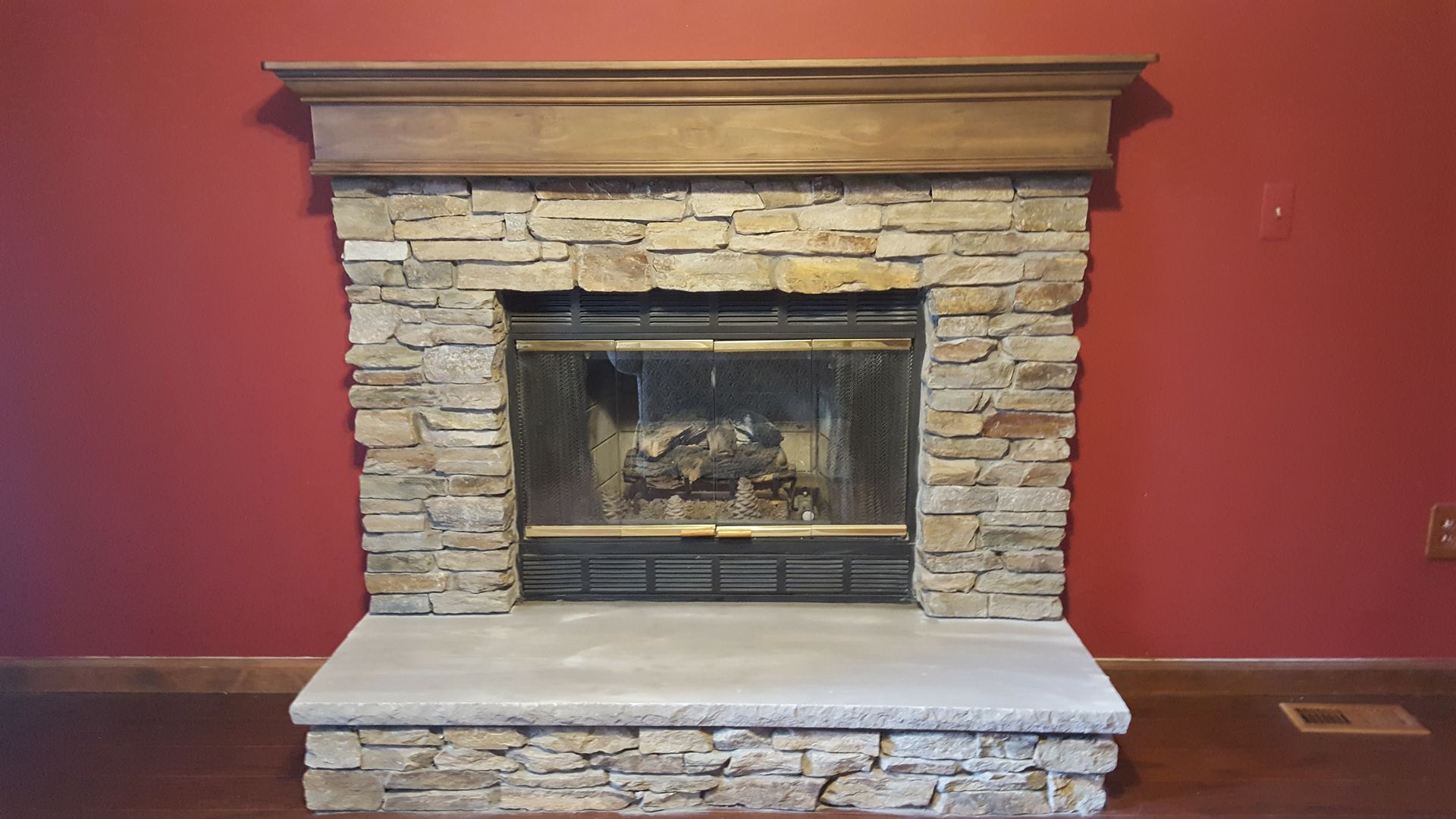 Stone fireplace with a wood mantel against a red wall, centered in a room.