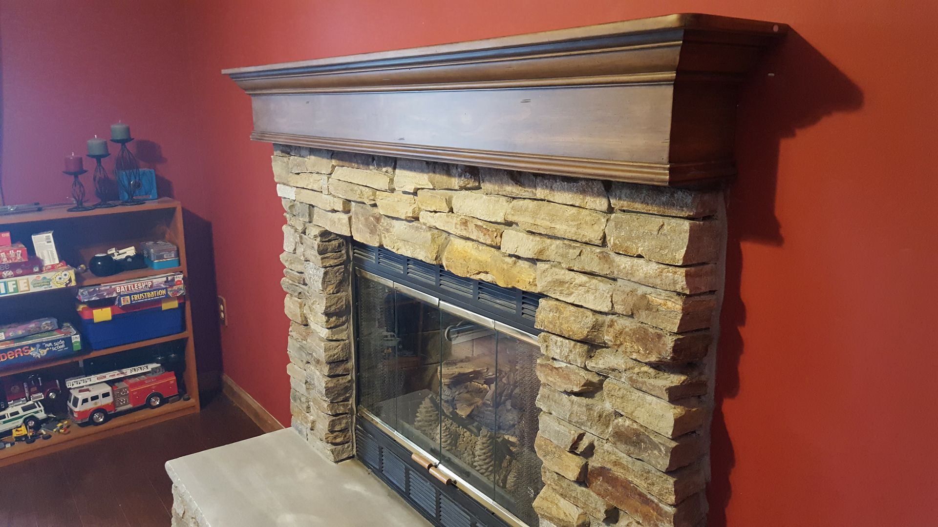 Stone fireplace with wooden mantel in a room with red walls and a small shelf of items nearby