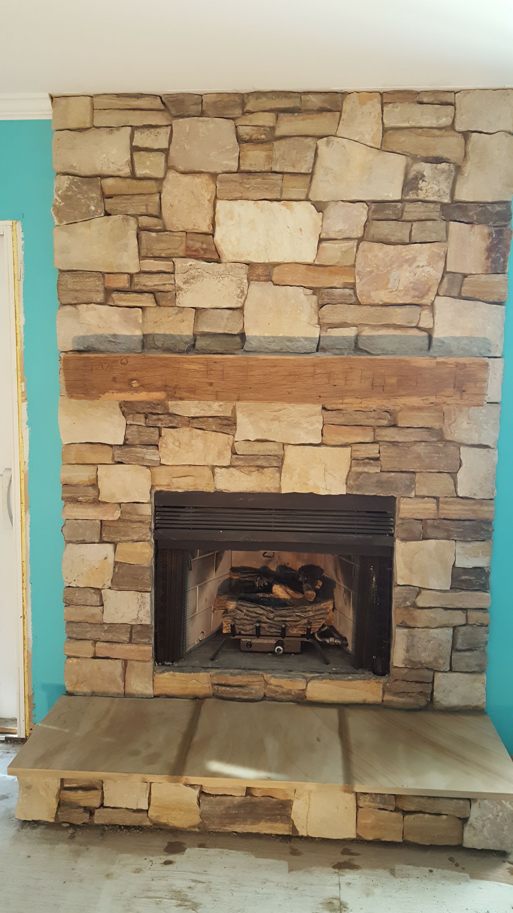 Stone fireplace with a raised hearth and black firebox, framed by a turquoise wall.