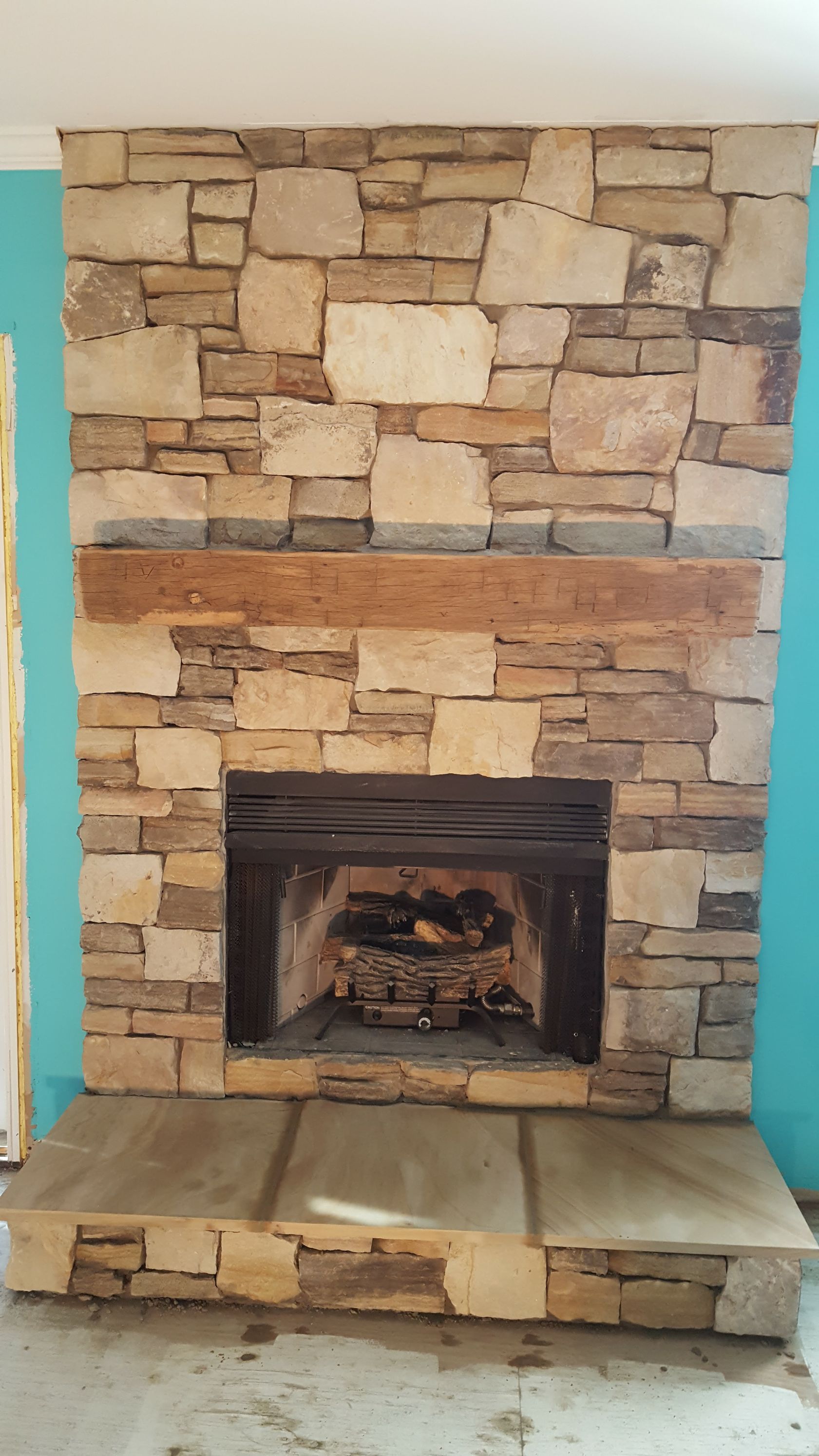 Stone fireplace with a lit fire and a raised stone hearth, set against a stacked-stone wall.