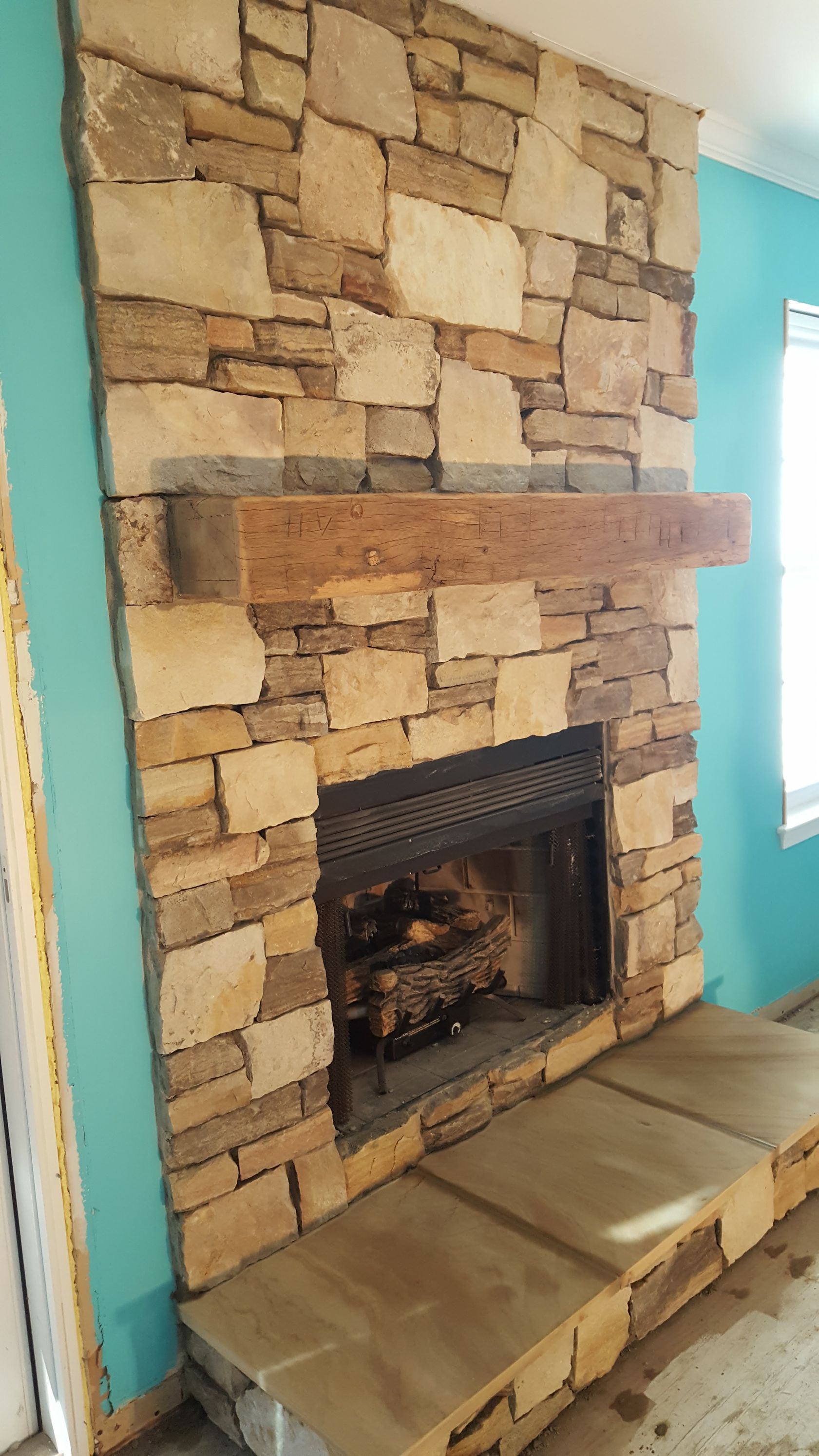 Stone fireplace with a wooden mantel and built-in hearth in a living room with turquoise walls.
