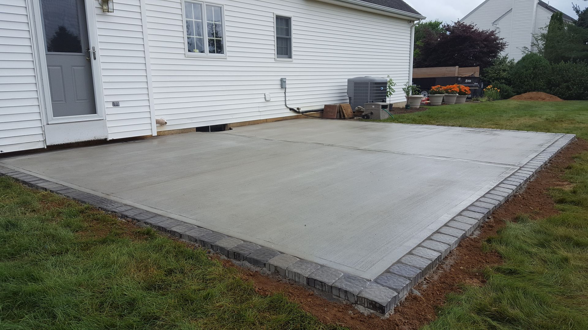 Concrete patio slab beside white house with brick edging and wet grass around it